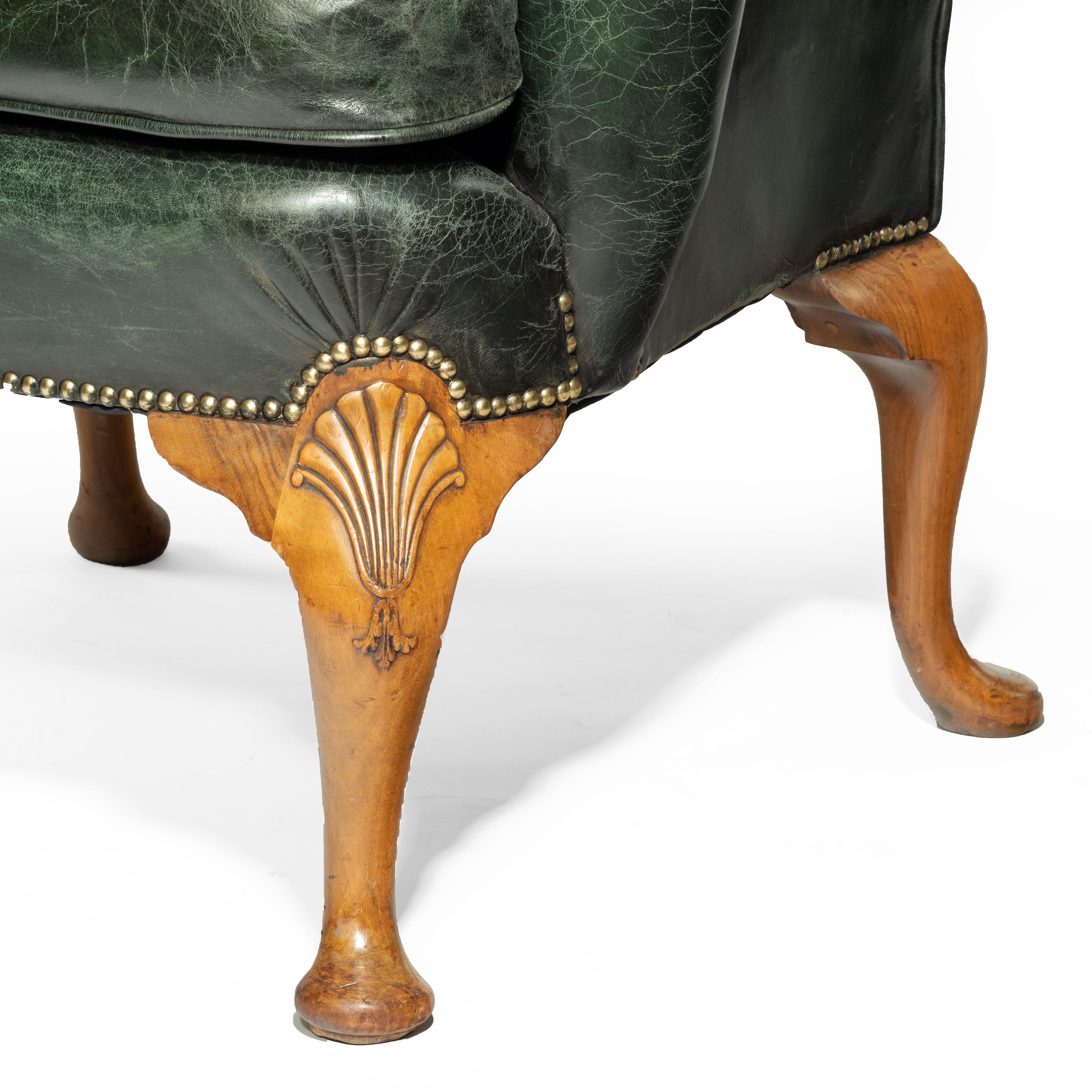 An Edwardian walnut wing armchair, of typical form with scrolling wings and arms, on four cabriole legs, the front knees carved with shells, re-upholstered throughout in distressed brass-studded green leather, English, circa 1910.

Measures: H 44in,