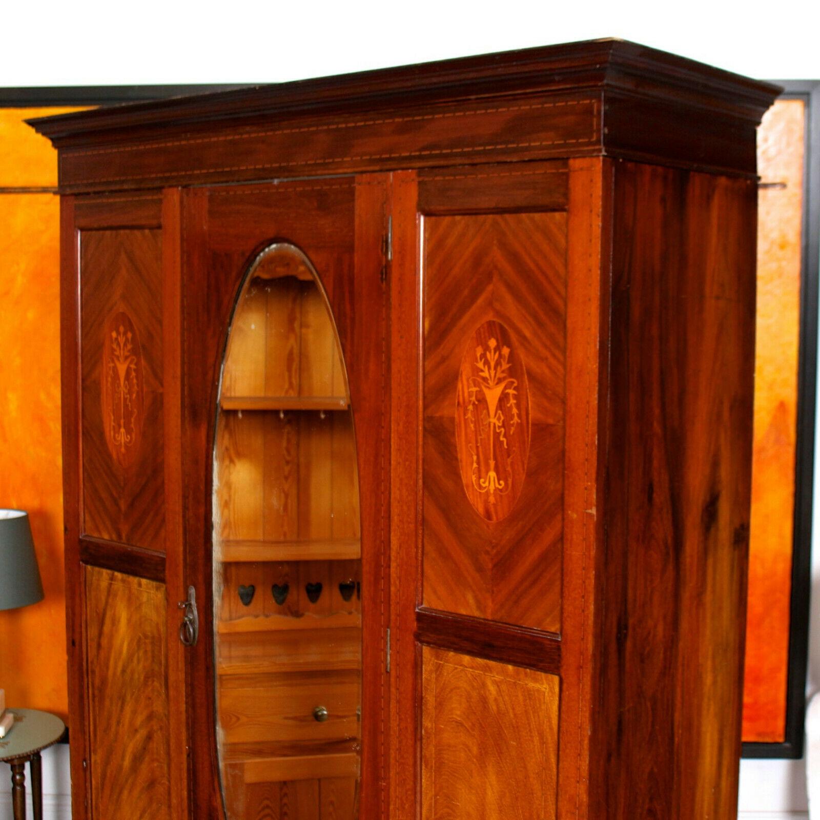 An impressive Edwardian period mahogany wardrobe.
An carved cornice above an oval beveled mirror paneled door flanked by inlaid Marquetry panels and enclosed hanging rails and storage. Fitted a drawer to based and raised on carved bracket