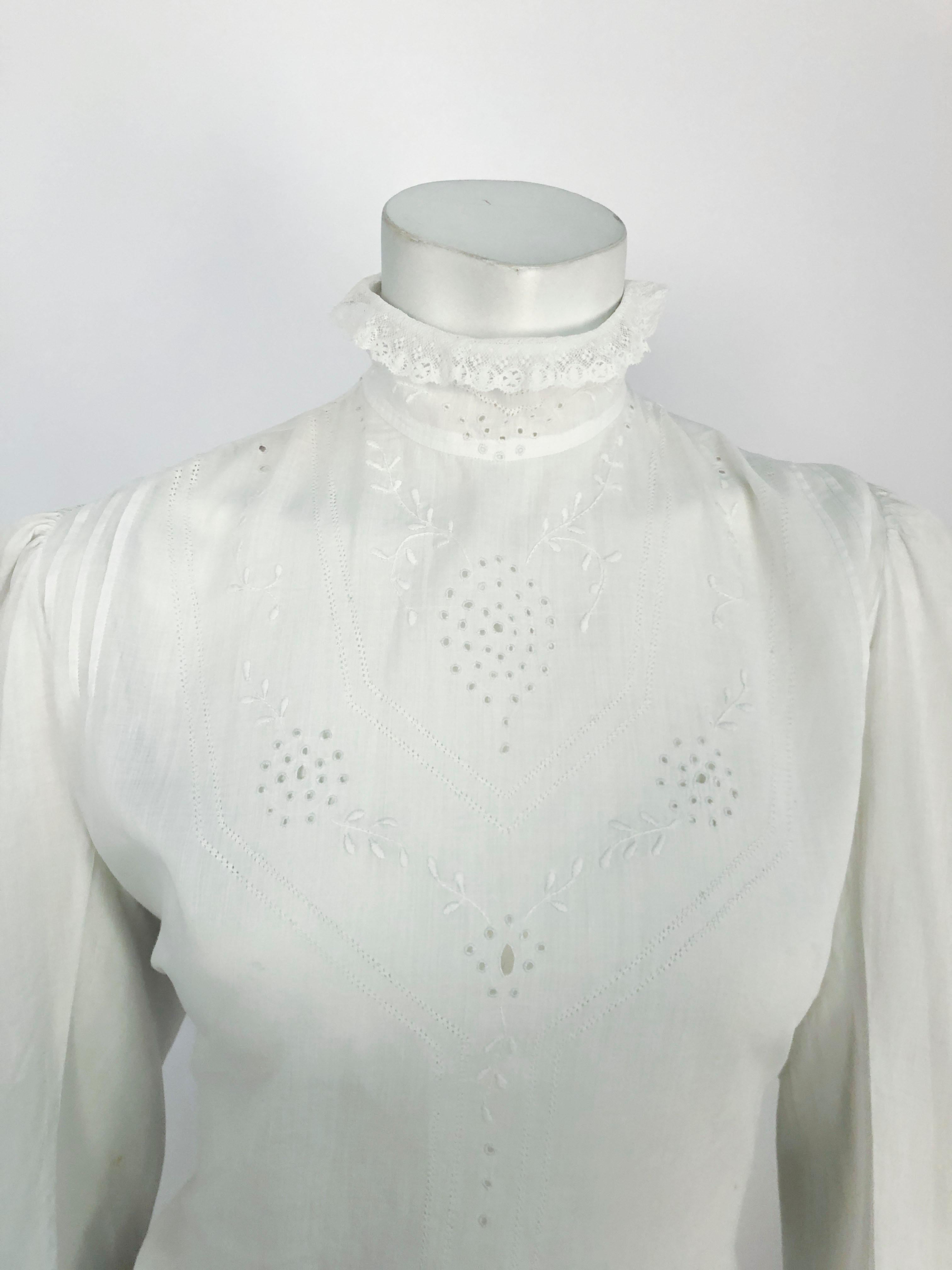 Edwardian white day blouse made of a thin lawn cotton with fine embroidery and pull work. There is lace trimming along the sleeves and high neckline. The waist is fitted with drawstrings that tie and traditionally hidden by skirt or sash. This piece