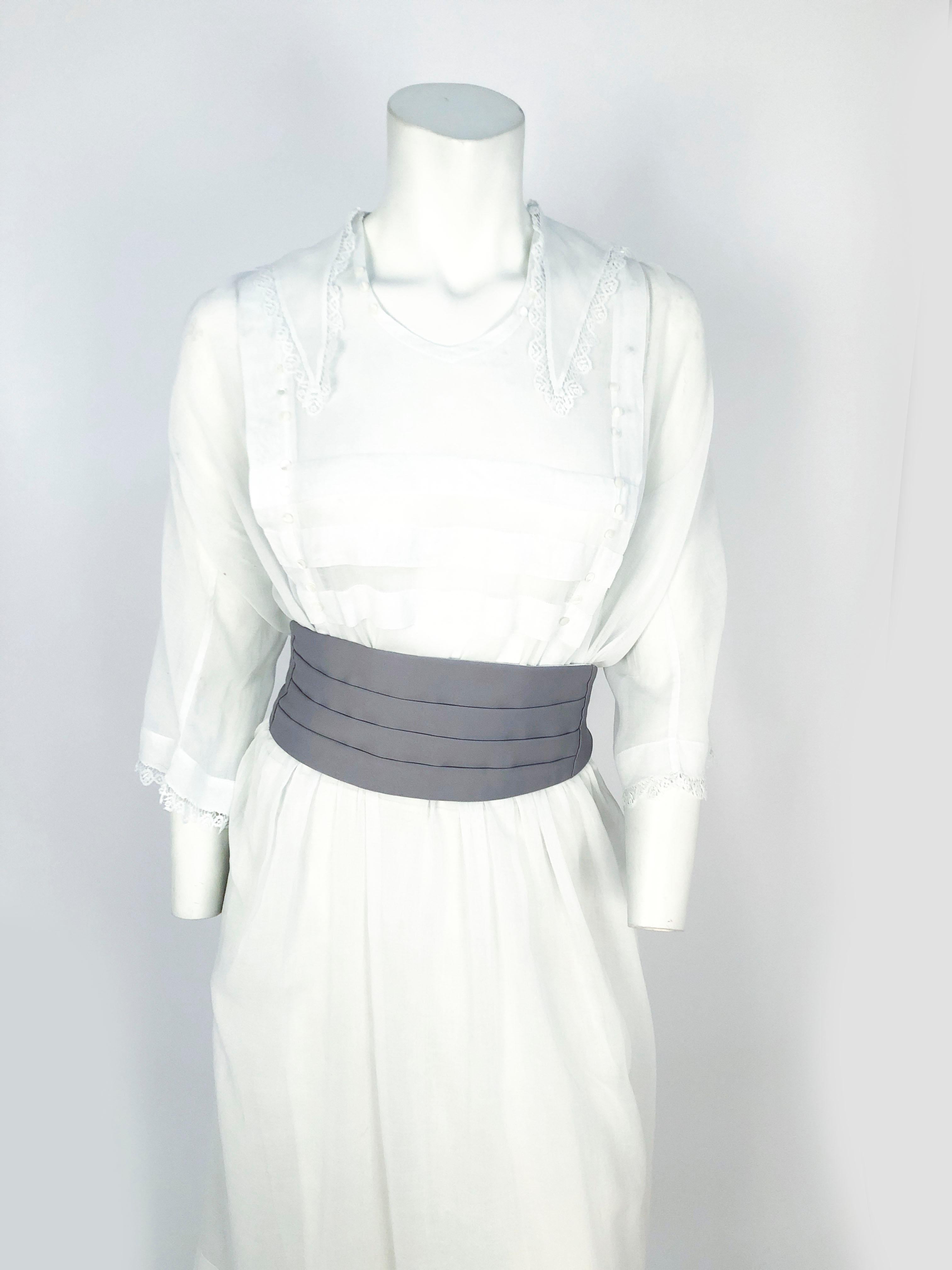 Edwardian white day dress. Made of a fine cotton with lace trim around the sleeves and the enlarged sailor collar. The bodice is adorned with wide pleats and seashell buttons. The waistline is gathered and the hemline is bordered with wide pleats.