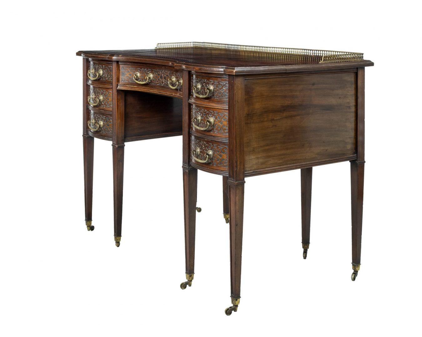 An Edwards & Roberts mahogany serpentine front ladies desk with leather inset top and cast brass gallery (a/f), with single frieze drawer and six flanking short drawers featuring Cope & Collinson locks and blind fretwork decoration, set on moulded