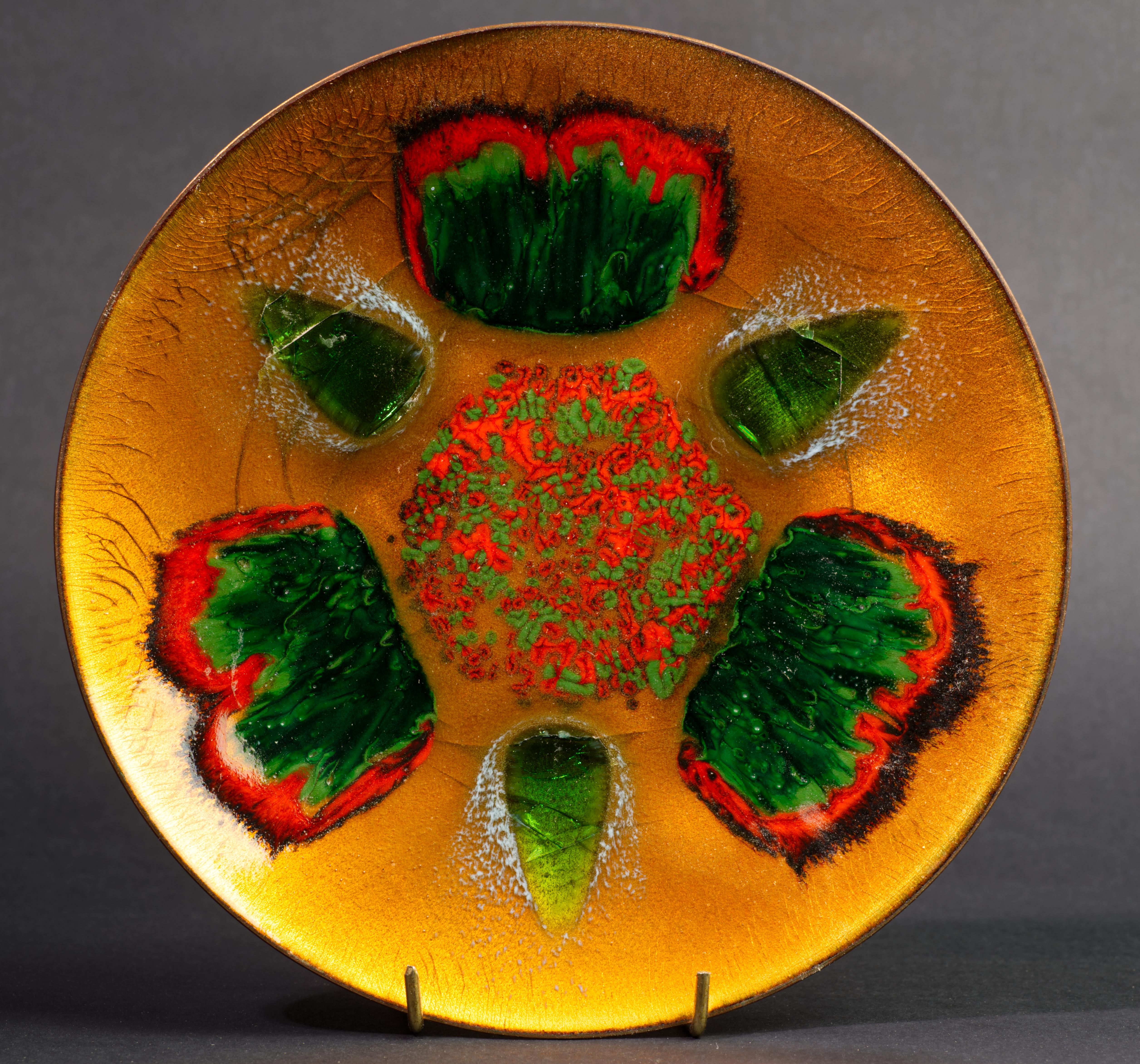  Cette magnifique plaque en laiton émaillée d'étoiles Edward, réalisée à la main, comporte trois détails en verre fusionné, d'un vert craquelé transparent, qui complètent l'émail vert malachite et orange brûlé utilisé dans le motif principal. La