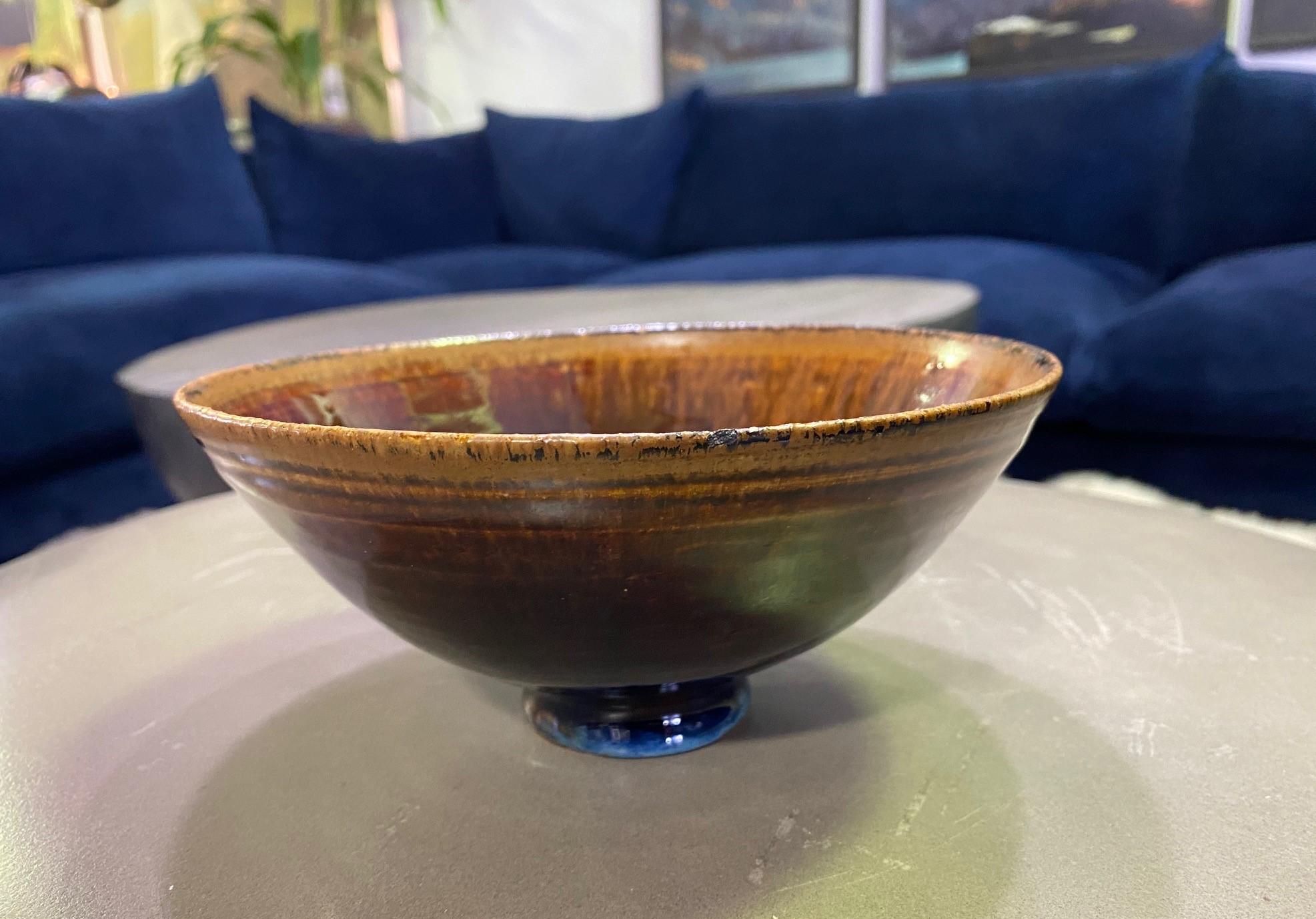 A gorgeously glazed pottery bowl by famed American master ceramist couple Mary and Edwin Scheier. The piece radiates in the light. 

The bowl is footed and has a beautiful brown-green tenmoku-like glaze. There is a smiley face at the center of the
