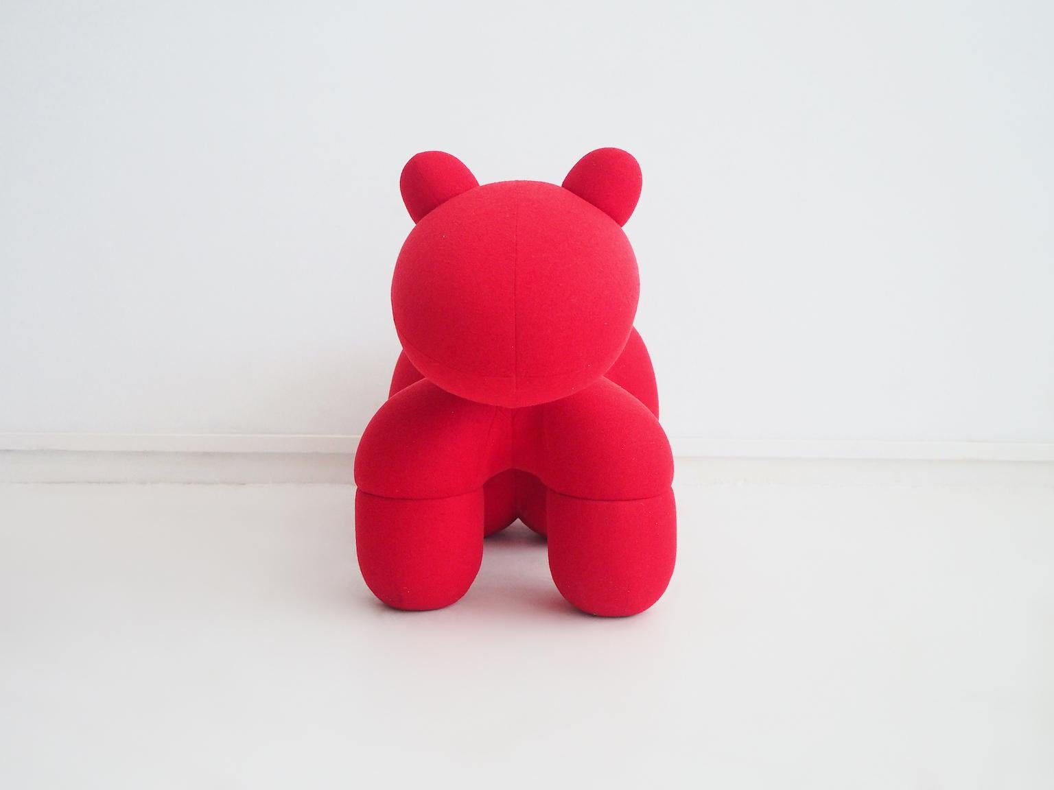 Fauteuil poney recouvert d'un tissu rouge. Ce siège emblématique a été conçu à l'origine par le designer finlandais Eero Aarnio en 1972. Il est doté d'un cadre en métal et d'un rembourrage en mousse, recouvert de tissu rouge. Il s'agit d'un siège à