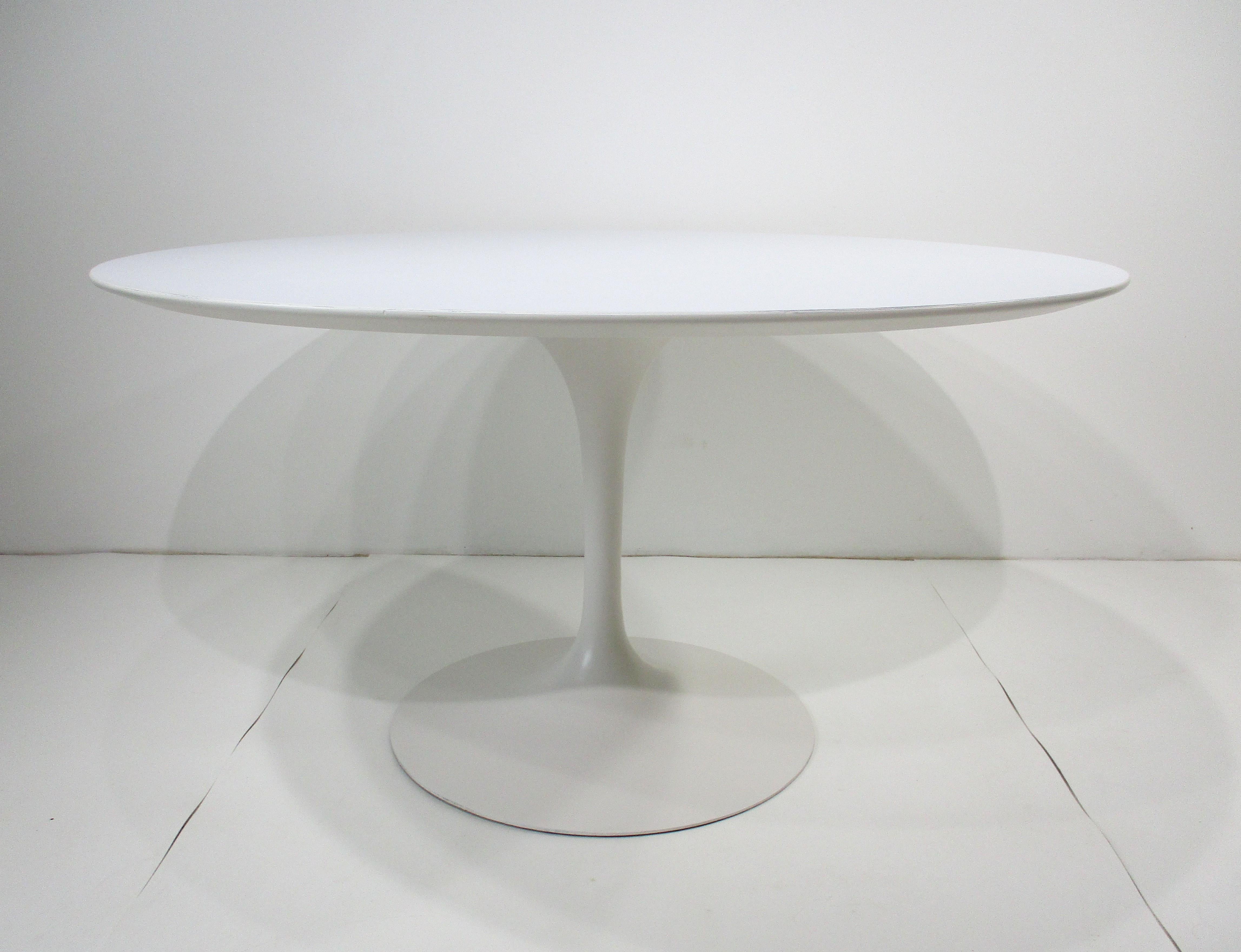 A early vintage round tulip dining table with white Laminate top sitting on a steel base . Designed by Eero Saarinen for Knoll this functional iconic dining table is a classic and works with any chair from mid century to traditional . Sized