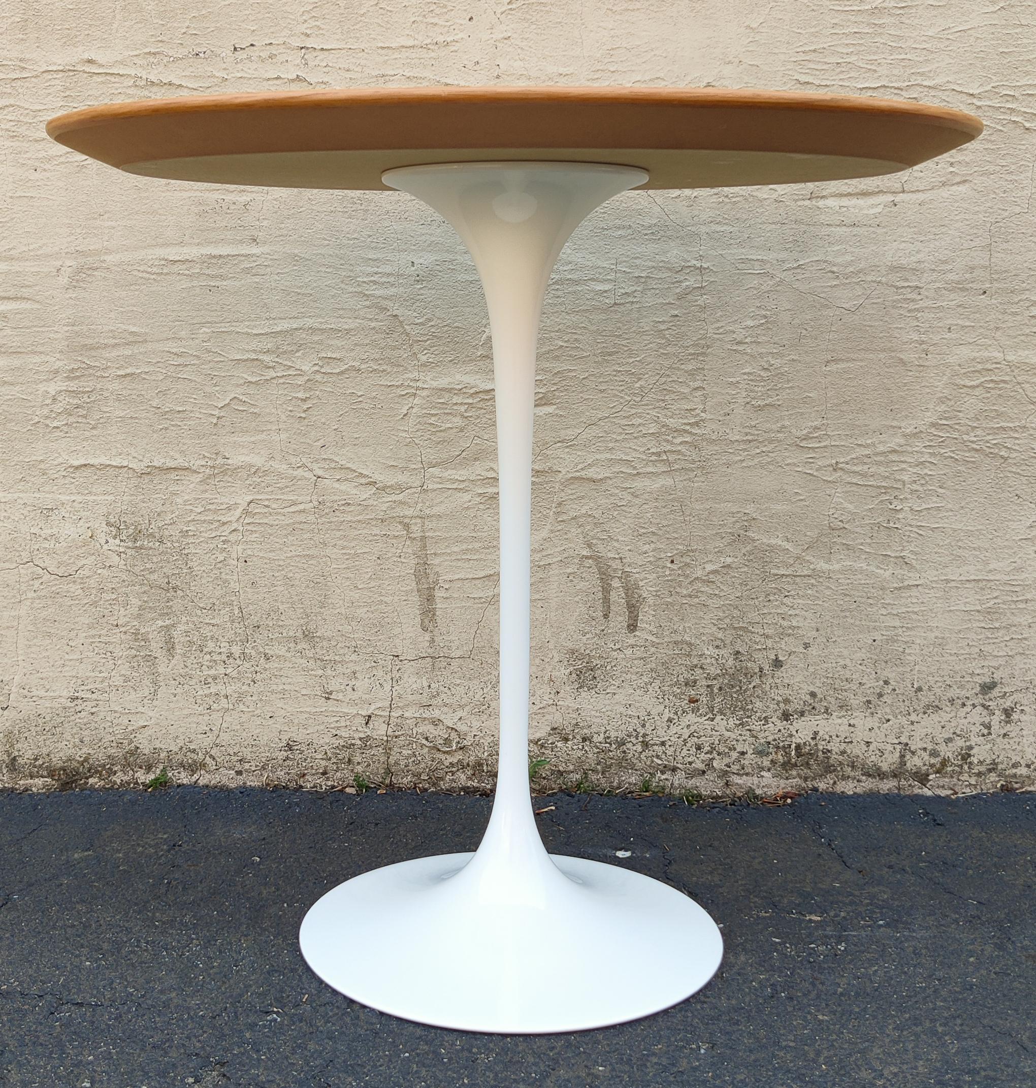 Designed by Eero Saarinen for Knoll in the 1950s, the Tulip line has expanded to many different tables and chairs. This example is a short and handsome side table make with a warm stained oak and a cast iron white enameled base. This contrast is