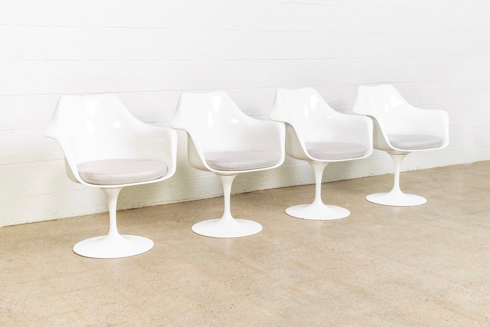 This set of 4 vintage mid century modern Model 150 tulip chairs was designed by Eero Saarinen and manufactured by Knoll. This iconic set of armchairs features a white molded lacquered fiberglass seat form on a 360 degree swivel cast aluminum