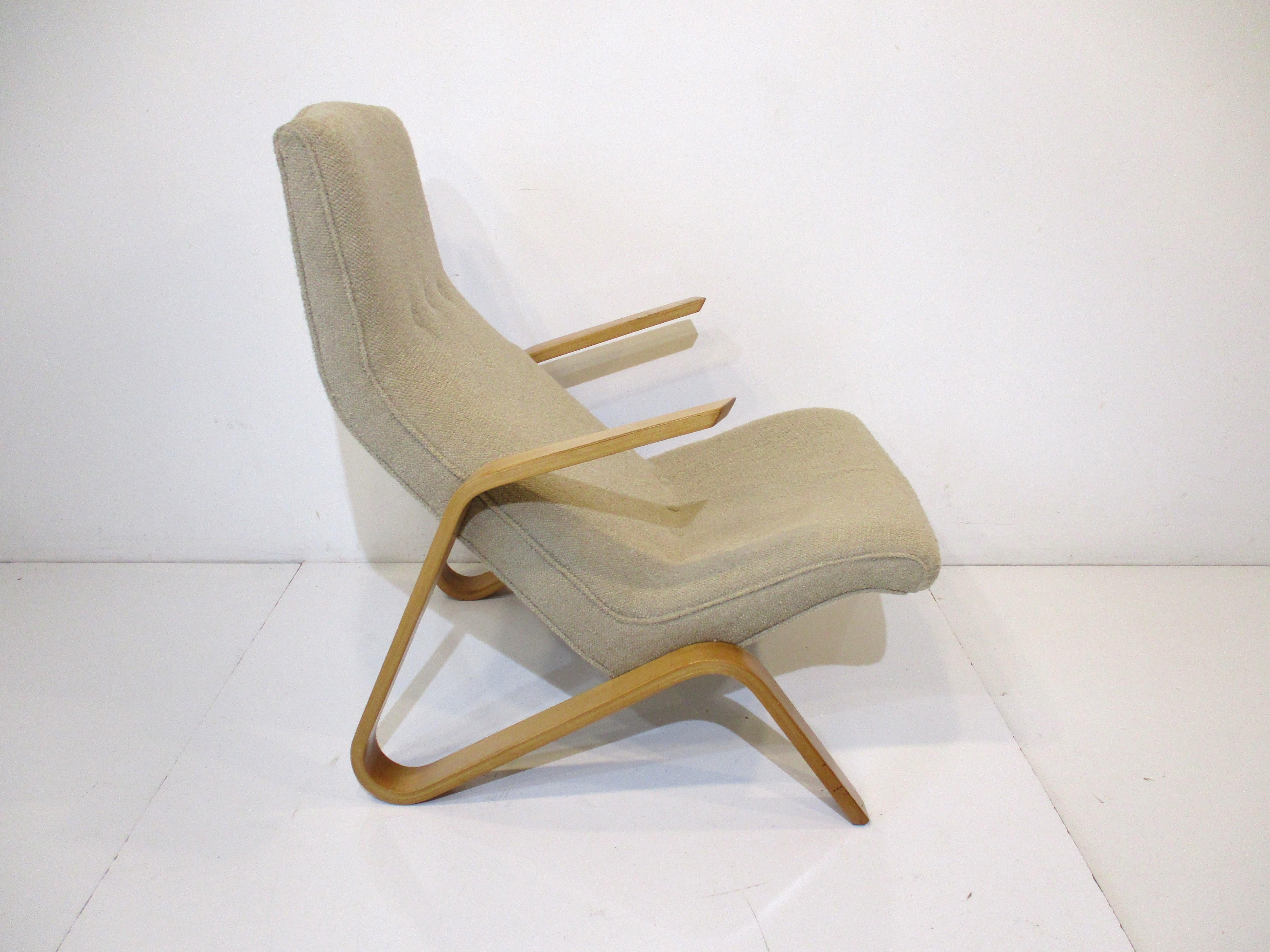 A early Grasshopper lounge chair with sculptural wood arms and a light taupe toned upholstery with button front. The bent wood arms are in a lighter birch wood and set at an angle with the high back and ergonomically correct sitting position for
