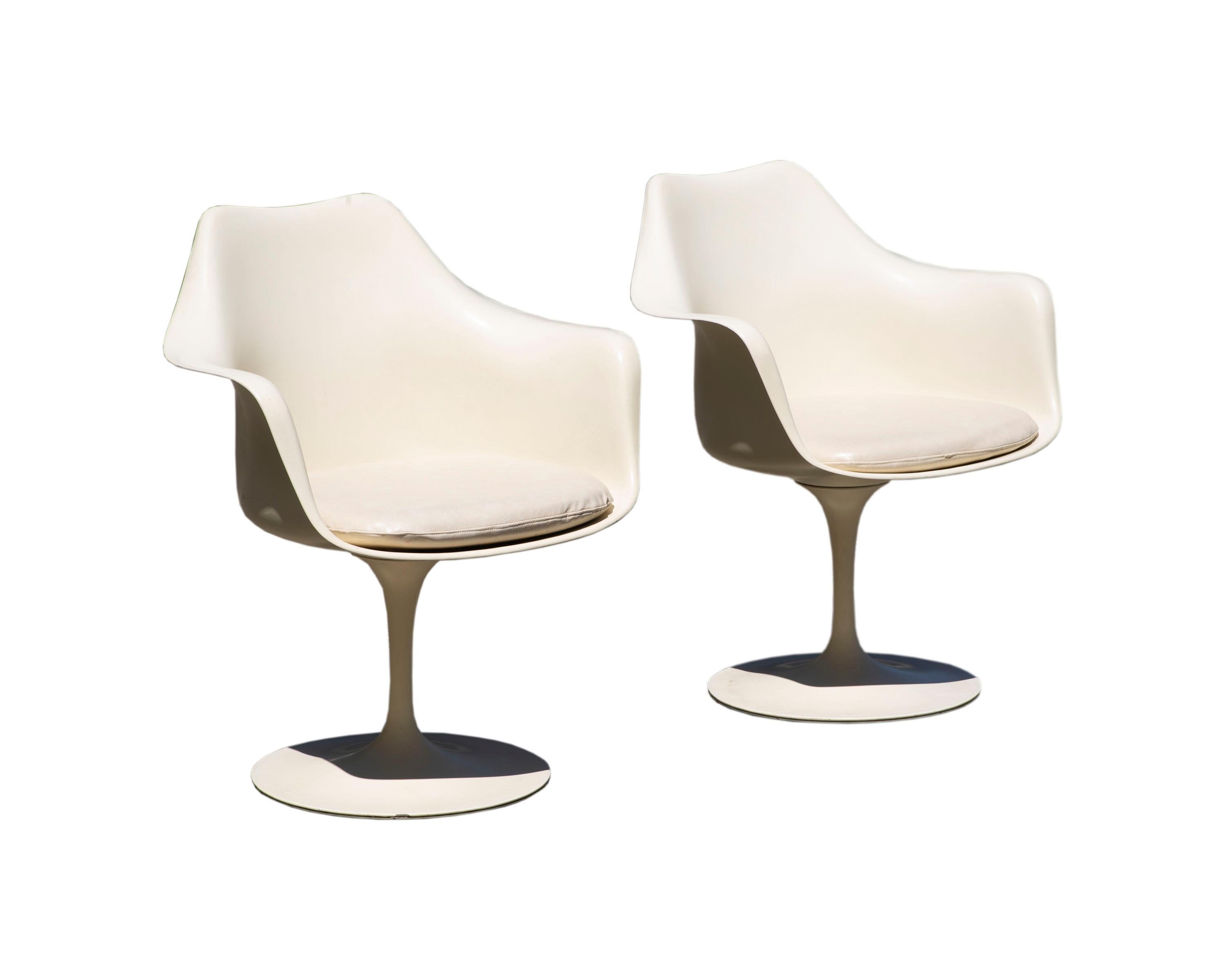 A pair of Tulip chairs designed by the Finnish-American Eero Saarinen. Produced by Knoll, these iconic Mid Century Modern chairs feature a fiberglass shell, a metal base, and the original vinyl cushions. Each of the chairs is marked with a Knoll