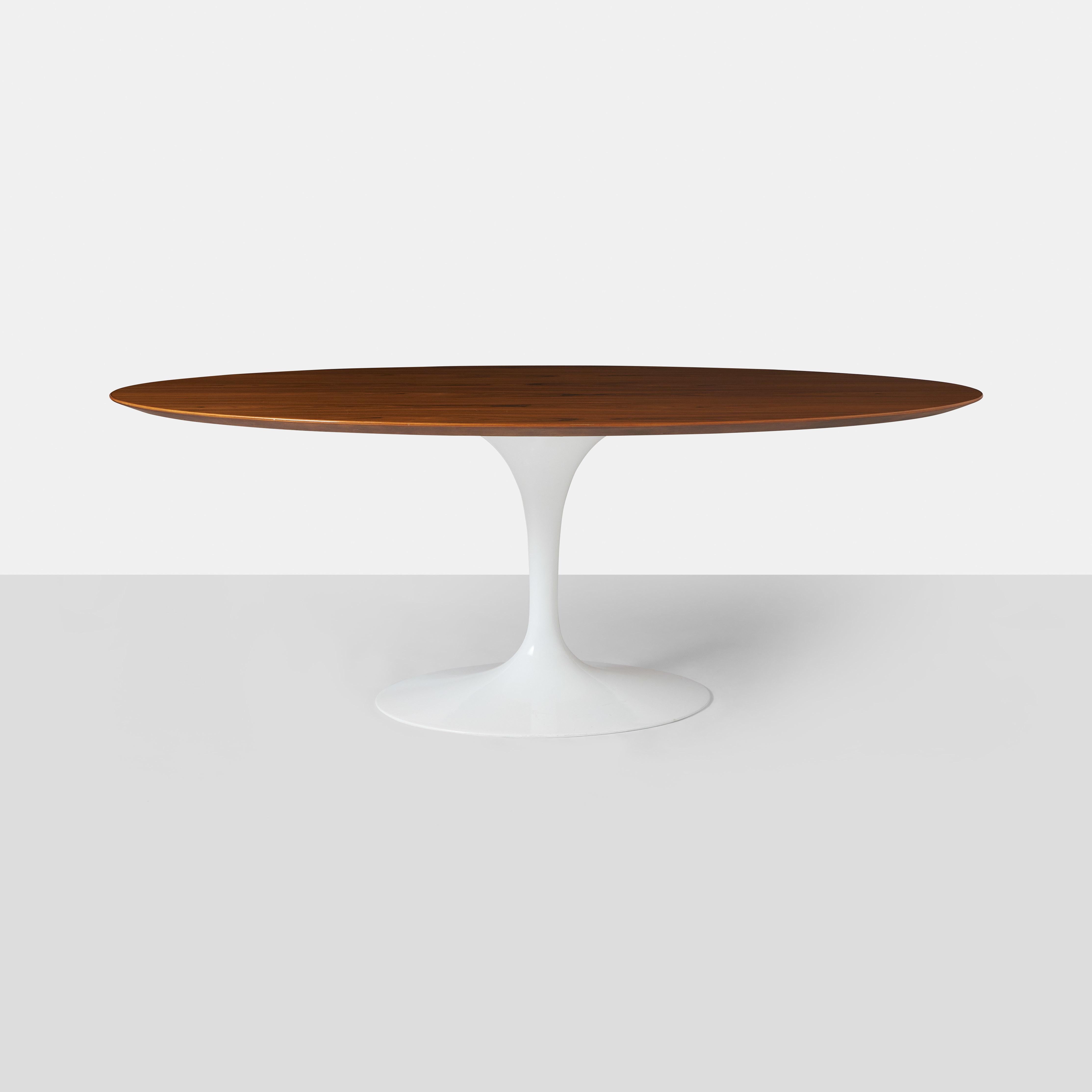 An oval walnut dining table from 2009 with a beautifully grained knife edged walnut top, a white cast aluminum pedestal base. 
Manufacturers label and metal Saarinen signature plaque on the underside.