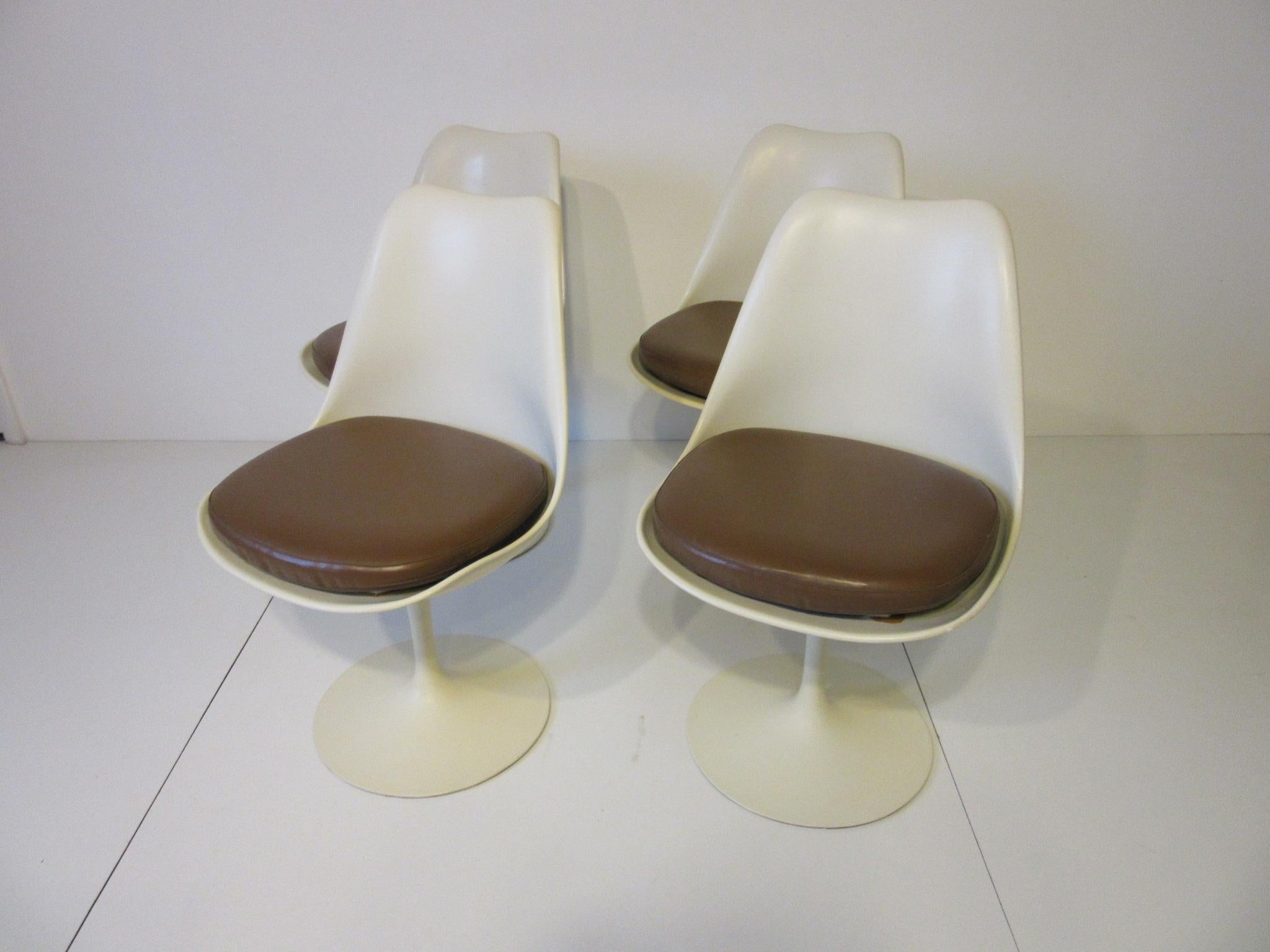 A set of four swiveling tulip dining chairs with toffee colored Naugahyde cushions, retains the manufactures labels and fabric tags made in the USA by Knoll.
 