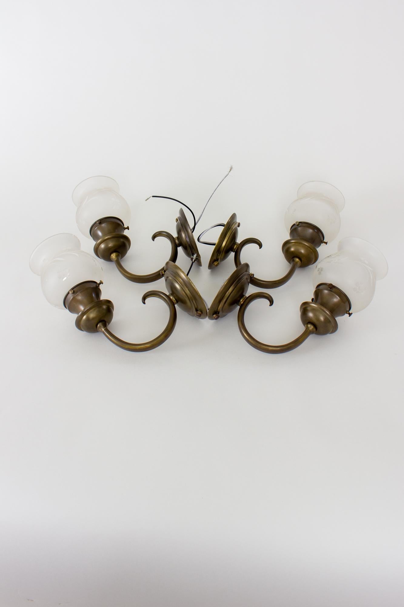 Brass E.F. Caldwell sconces with etched glass shades - set of four. Round backplates with upcurled arms, bobeche and cup shaped shade holder. Original dark patina has been cleaned and restored. The glass is a flared cup shape, etched with a classic