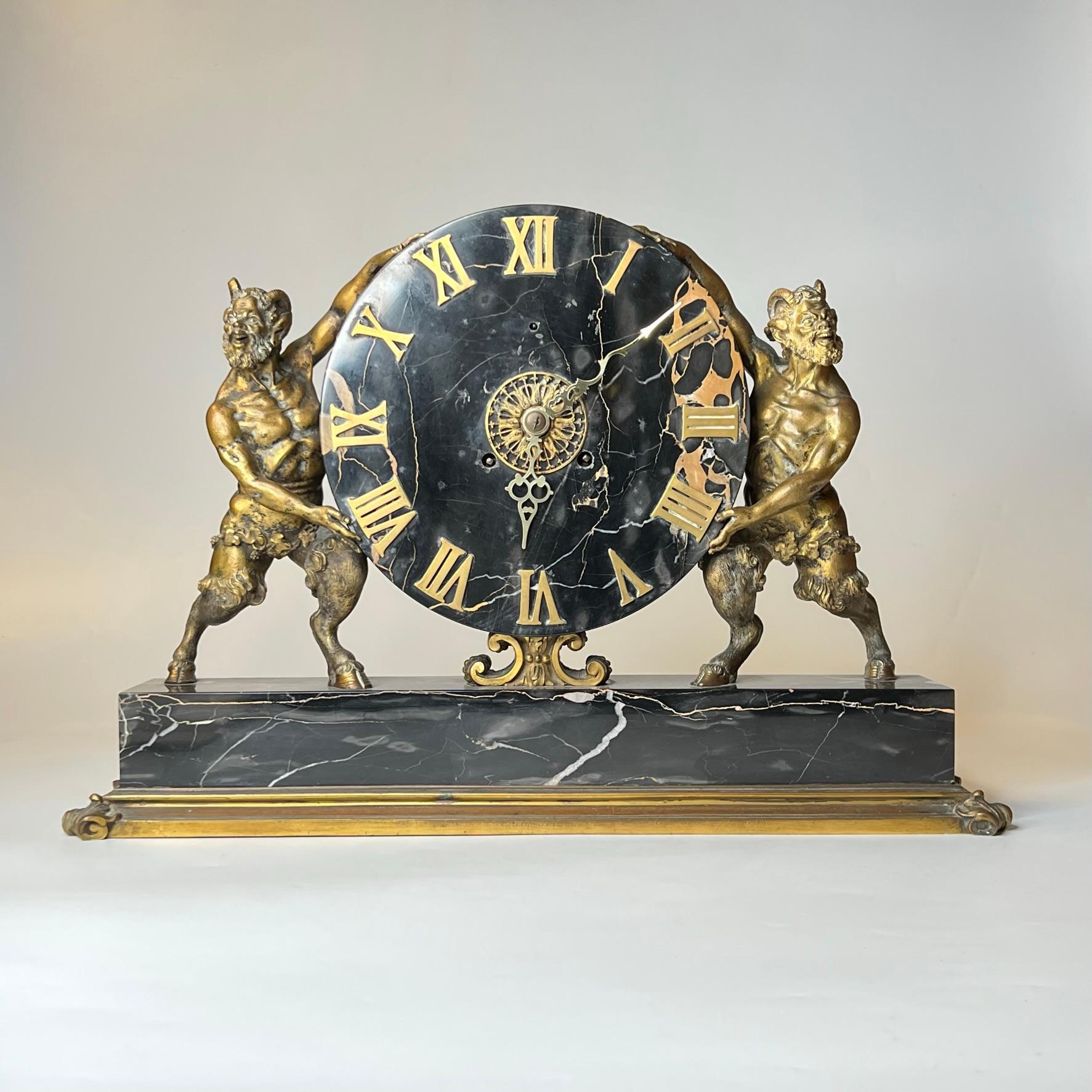 Our mantel clock in the Greek Revival style is crafted from marble and gilt bronze and features a large dial with Roman numerals supported on each side by satyr figures. Signed on the reverse. In good condition.