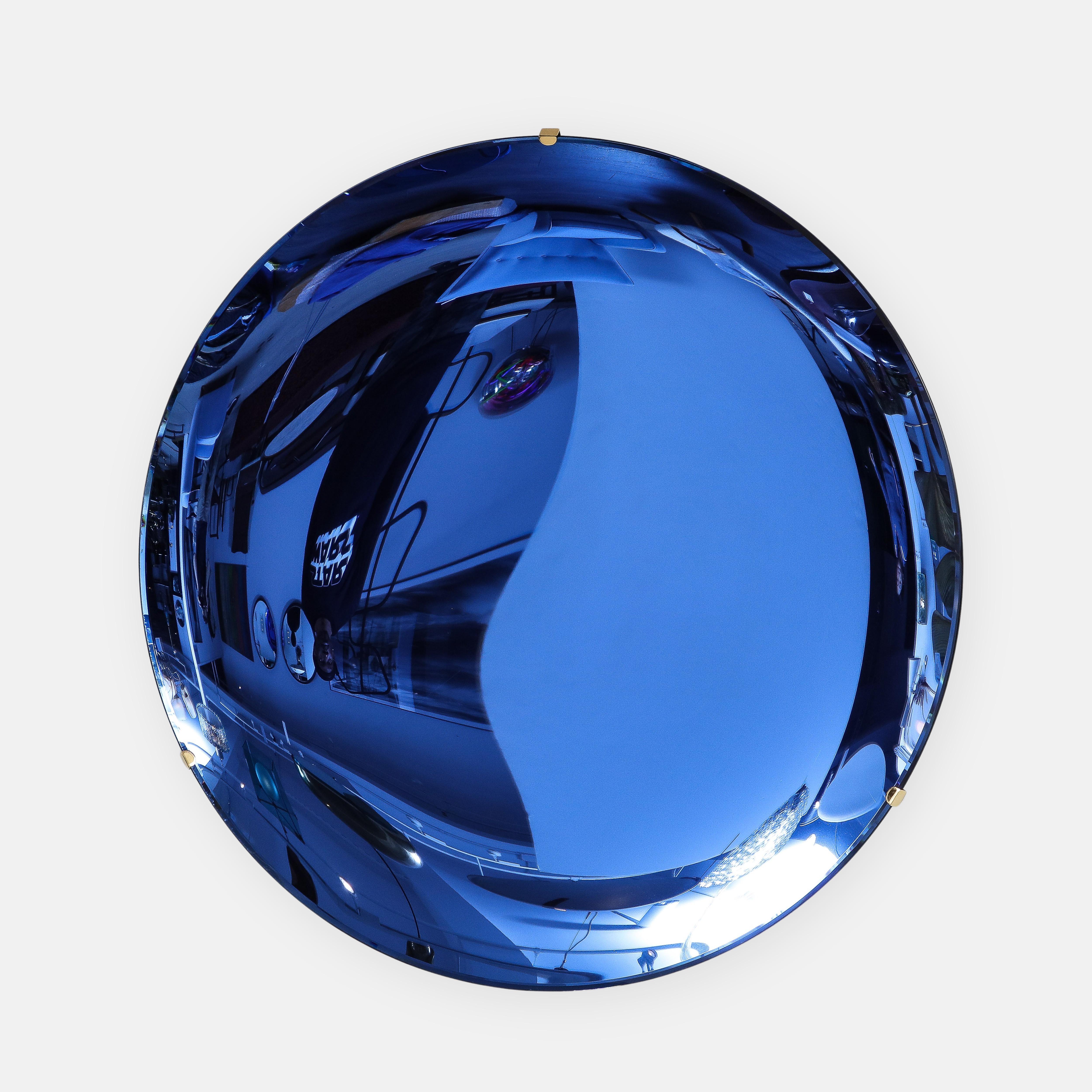 Effetto Vetro contemporary large round concave cobalt blue colored mirrored glass mounted on a polished brass structure on the back with three mounting clips on the front edges, Italy, 2022. This exquisite mirror is a sculptural work of art, grand