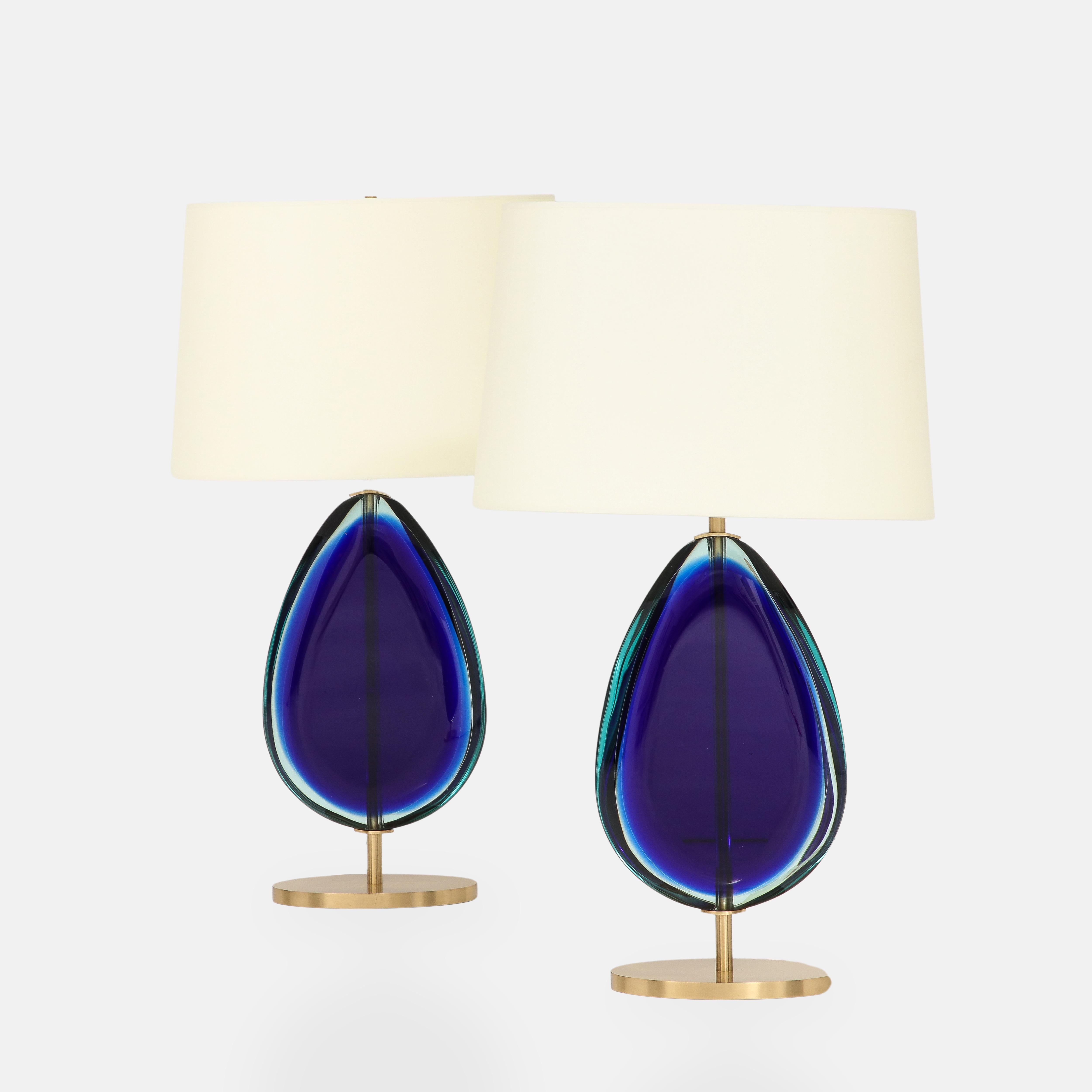 Effetto Vetro contemporary pair of table lamps each with large shaped blue glass in teardrop form suspended from satin brass stem and oval base with oval ivory paper shades.  These lovely and elegant table lamps are handmade and require intensive