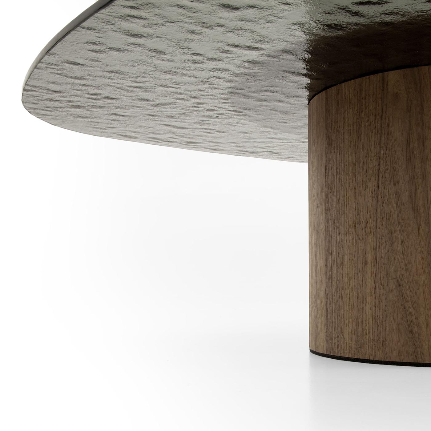 Se distinguant par son élégance moderne, cette table basse témoigne d'un design sophistiqué. Avec sa base cylindrique fabriquée en MDF plaqué noyer Canaletto, il respire le luxe intemporel. Le plateau en verre fumé martelé semi-transparent ajoute un