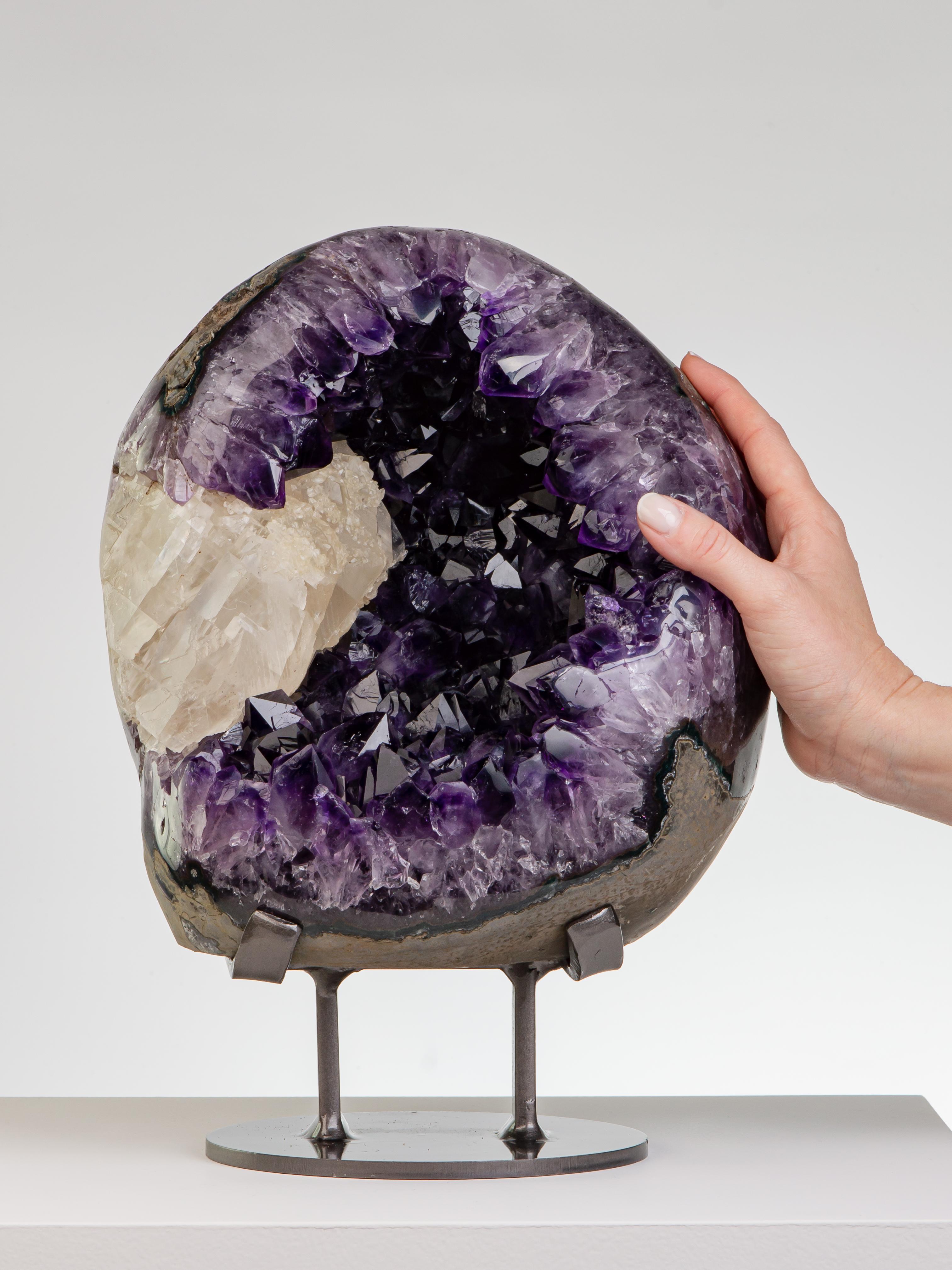 A beautiful mostly complete egg shaped geode with a prominent calcite
to the left, partially polished. The amethyst crystals with high peaks and
of intense purple. The thick amethystine borders polished.

This piece was legally and ethically