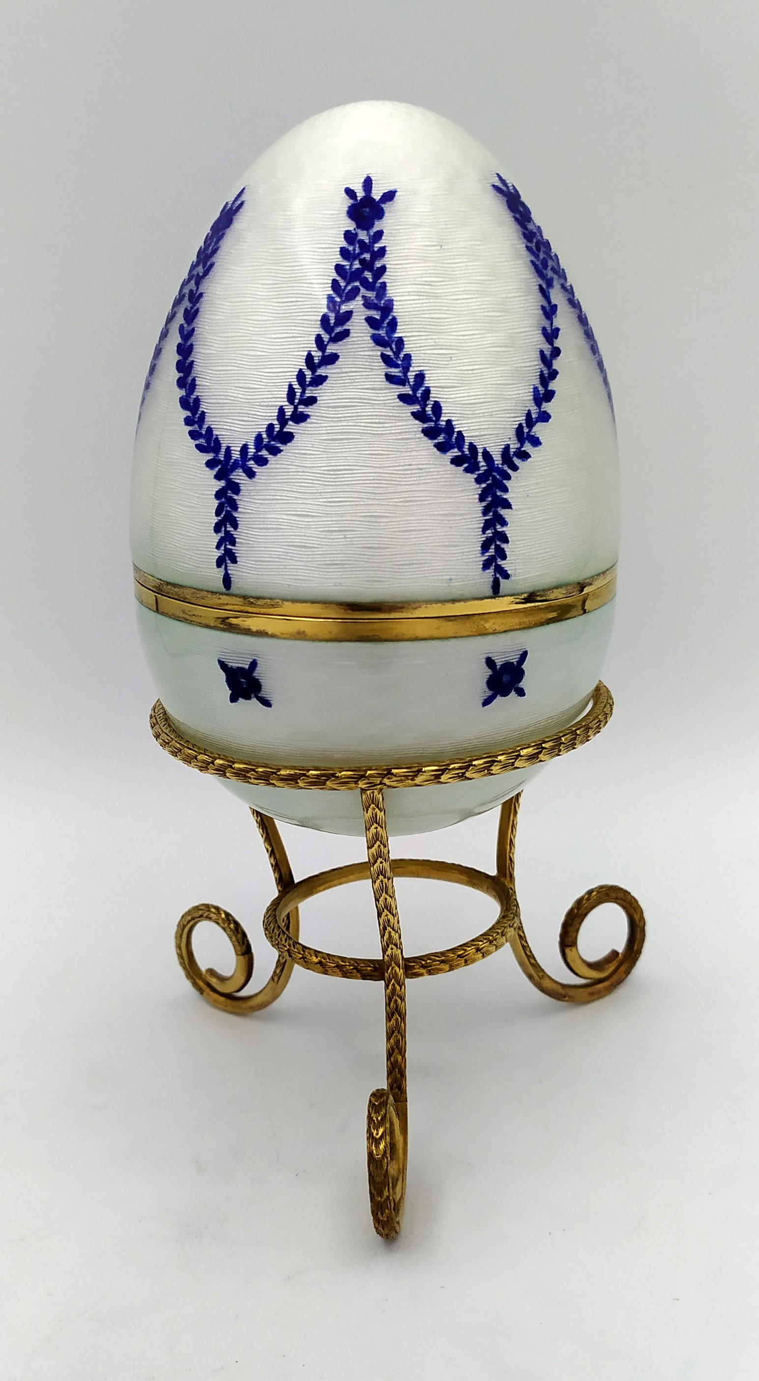 

Egg White with blue garlands is in 925/1000 sterling silver.
Egg White with blue garlands has fired enamels on guilloché and design engraved by hand.
Egg White with blue garlands is on tall tripod with laurel.
Egg White with blue garlands is in