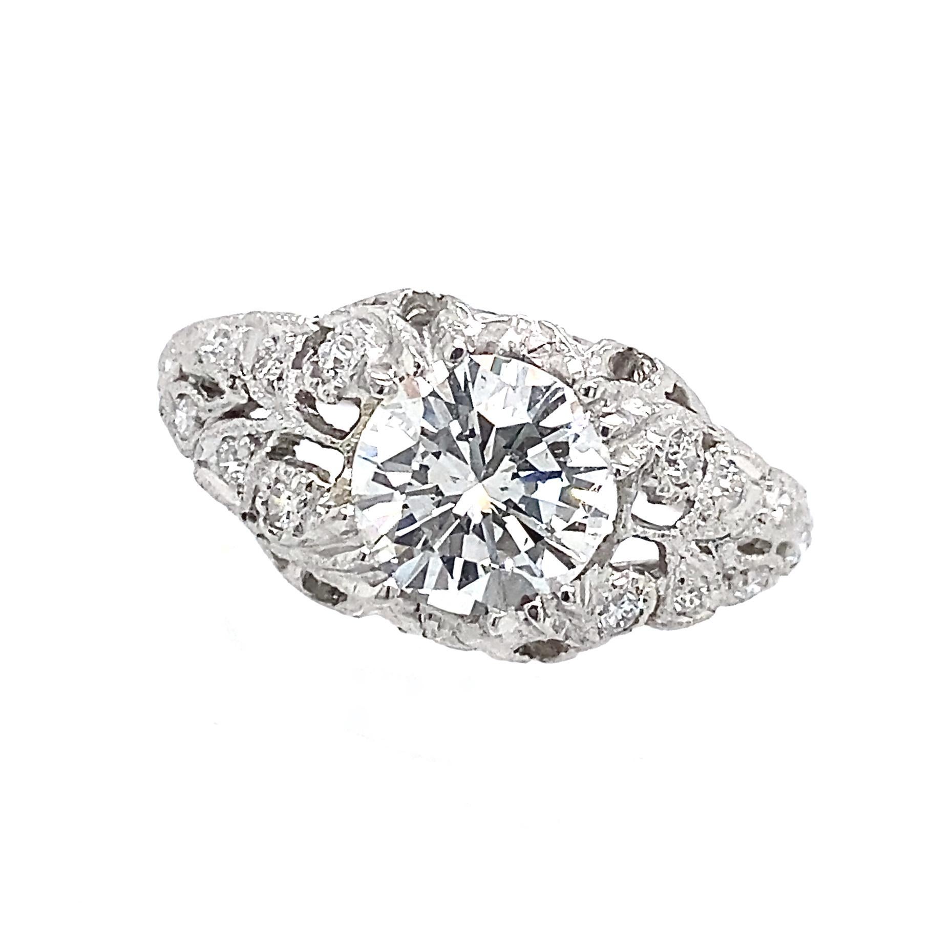 Eytan Brandes drew on elements of various Edwardian rings -- the leafy motif, the coin-edged foliate plates, the rising silhouette -- to create this lovely platinum engagement ring.  

The center diamond has an older (2002) EGL certificate