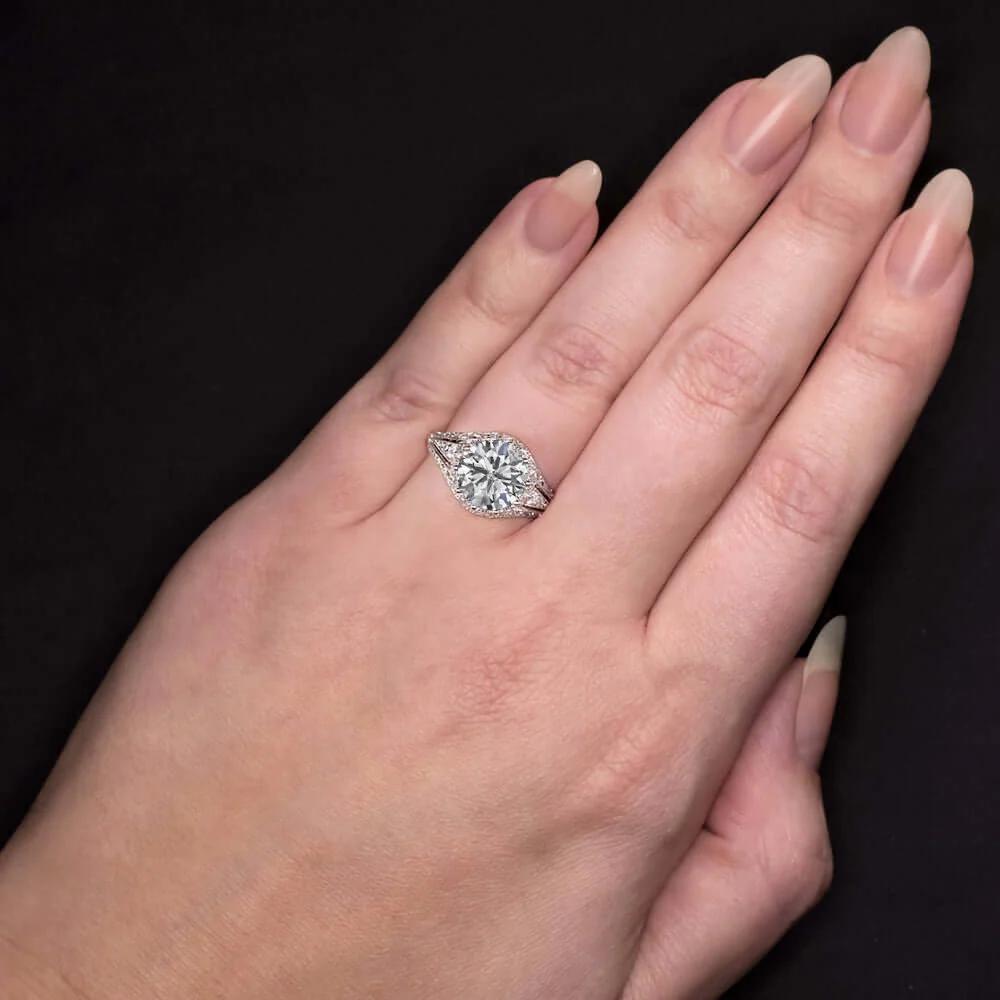 This exquisite vintage-inspired diamond ring showcases a stunning 2.55 carat round brilliant diamond certified by EGL-USA. The center stone features an exceptional D color and I1 clarity, with inclusions that are well hidden and blend with its