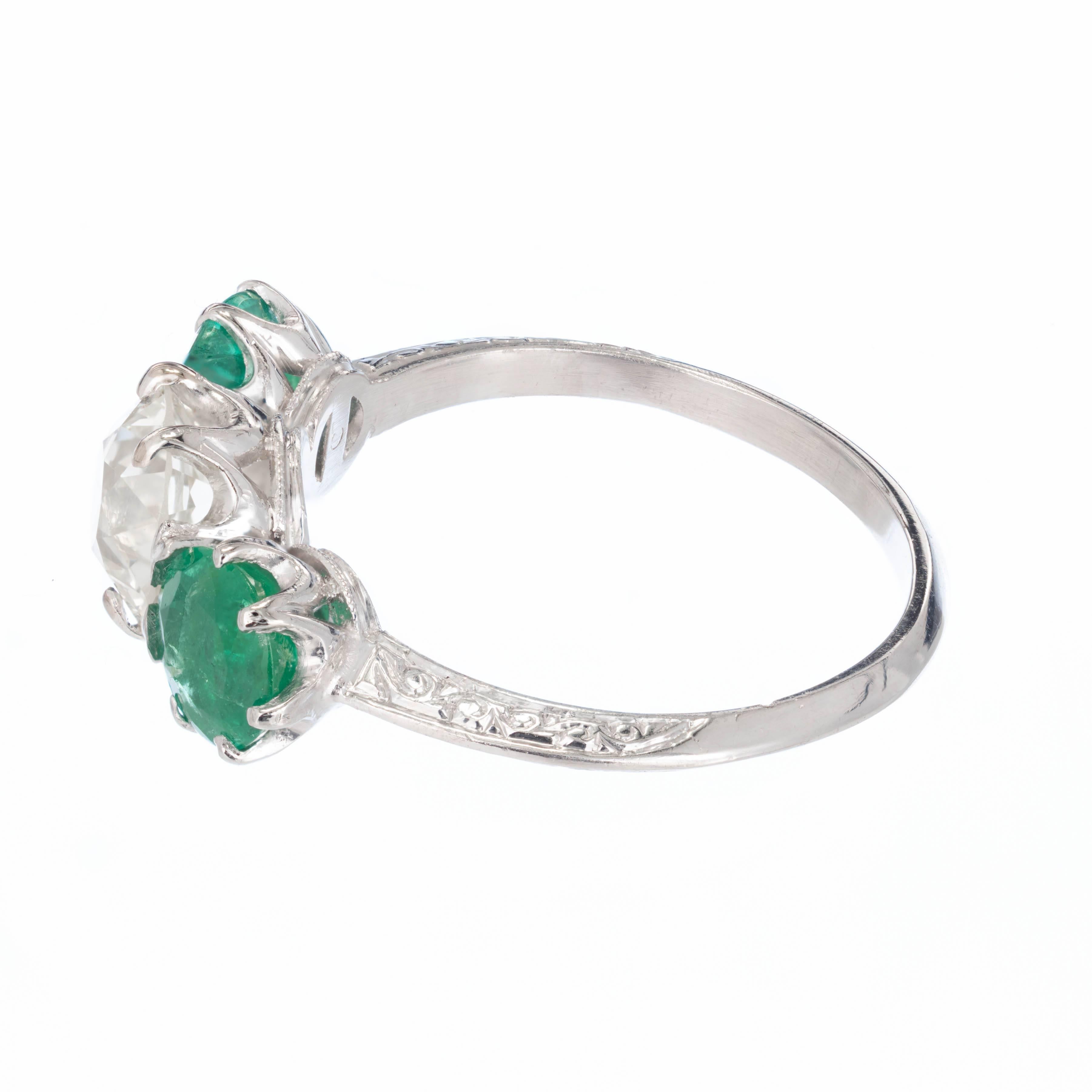 Art Deco diamond and emerald engagement ring. delicate engraving and pierced work. Old European cut round diamond extremely bright and well cut, with two bright green emeralds on each side. Moderately clear and moderately included. The color of the