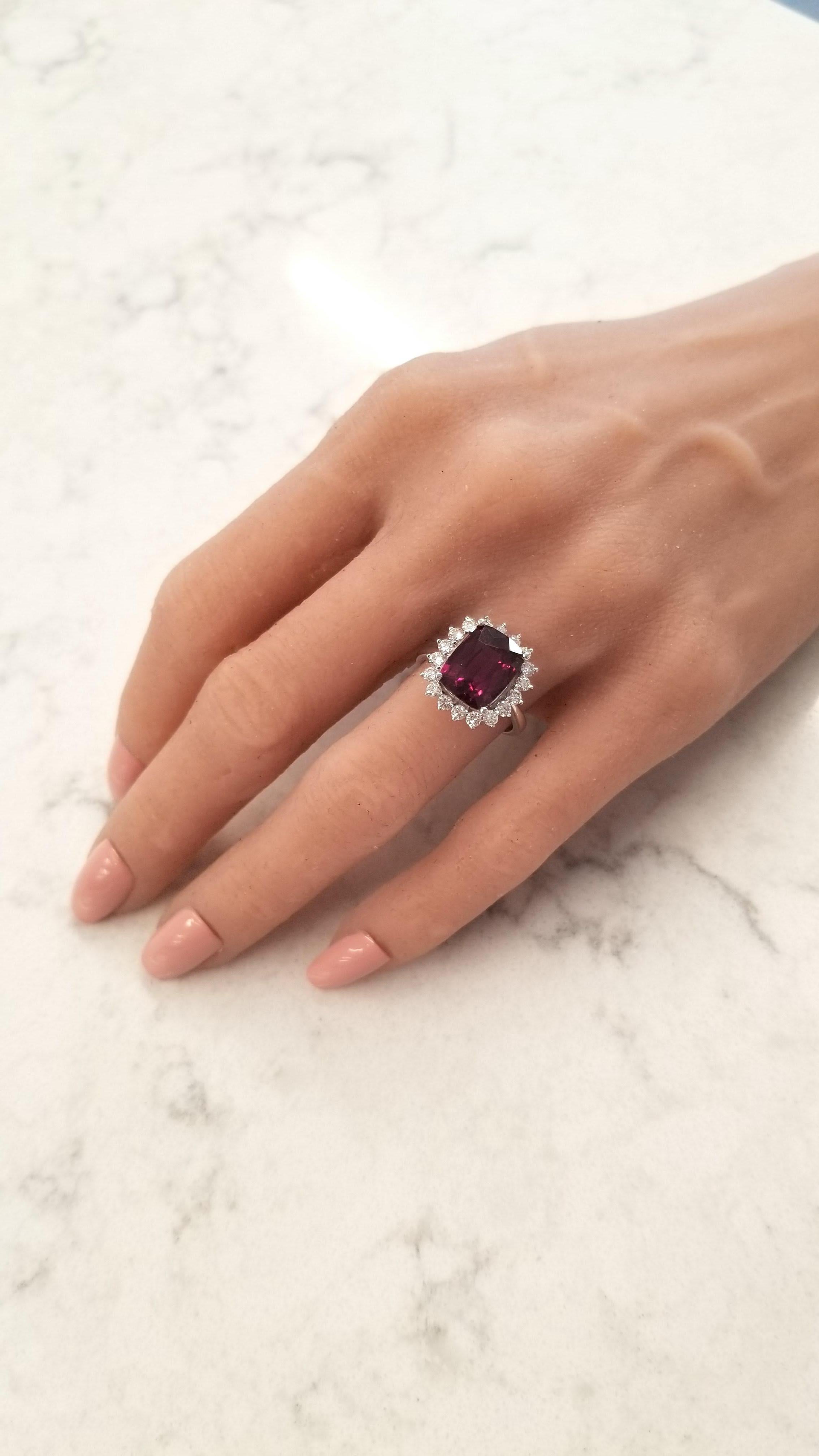 This gem ring features a 5.14 carat cushion cut rhodolite garnet. It measures 11.36 x 8.55mm. Its gem source is Sri Lanka and its color is intense raspberry. Its transparency and luster are excellent . A total of 18 scintillating round brilliant cut