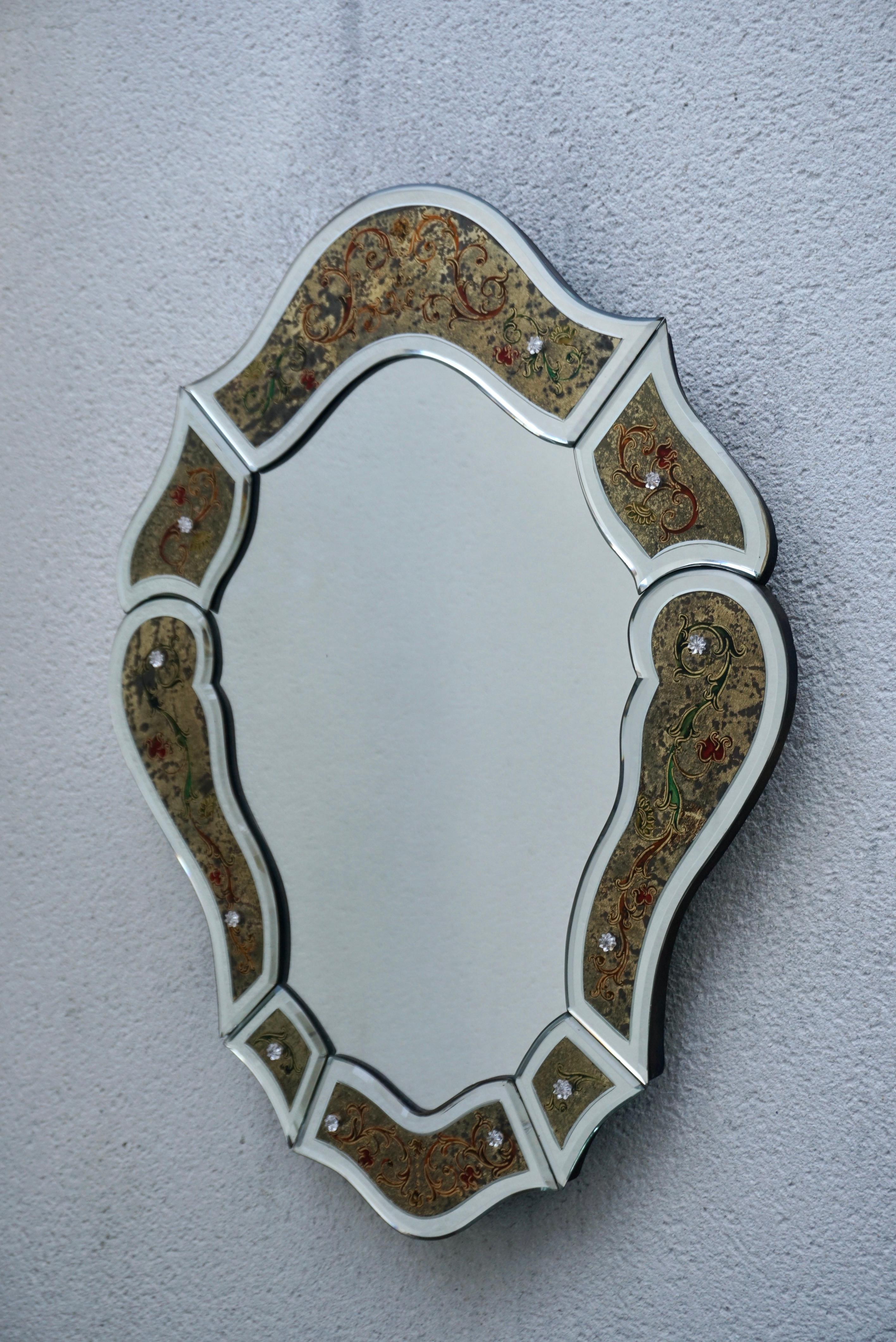 A beautiful venetian wall mirror featuring a mirrored frame with gold leaf églomisé detailing and a hand painted floral and scroll design. Italy, 20th century.