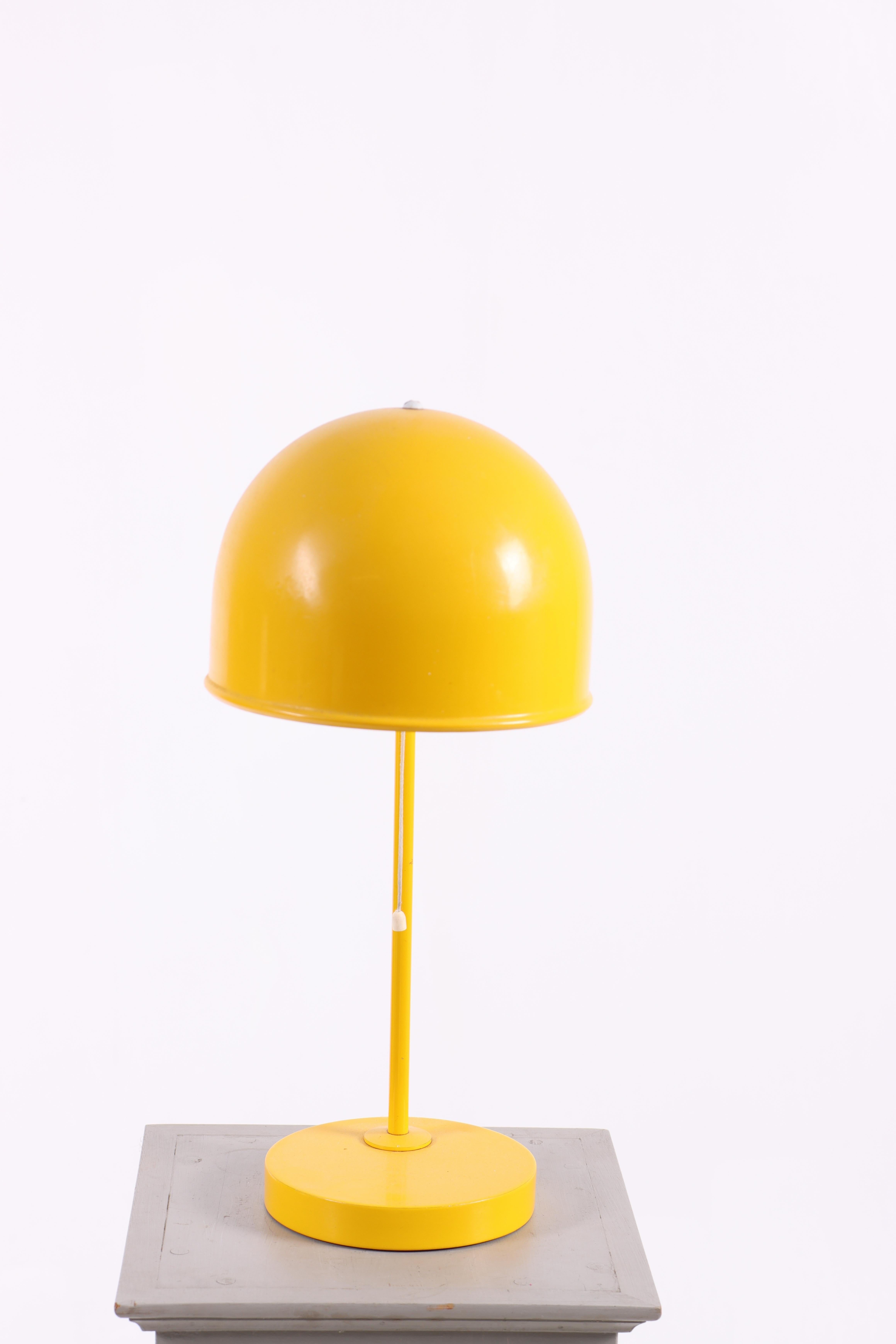 Lámpara de mesa amarilla, modelo B-075, diseñada por Egon Ahlgren y producida por Bergboms en Suecia durante la década de 1970.
La lámpara presenta una característica pantalla semiesférica montada sobre un esbelto tallo con base circular. El