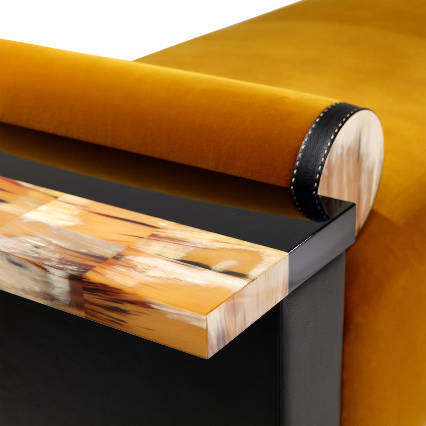 The Egon chaise longue is upholstered in Monsieur Baudelaire fabric in ochre yellow. The armrest is made of Aida pebbled leather in black Onyx, with an arm table of horn and wood in lacquered black gloss. The base is black lacquered wood with a