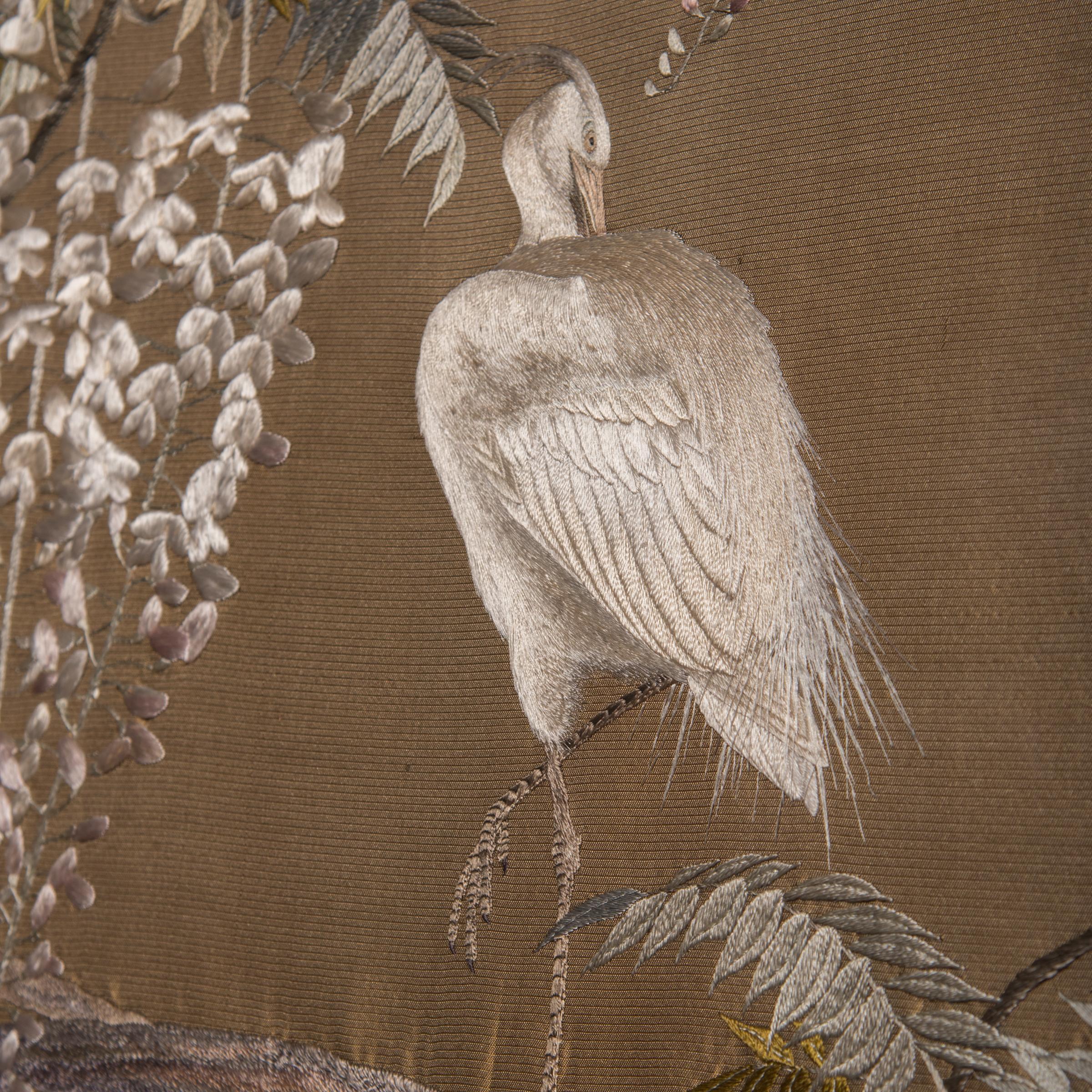 An exquisite example of Meiji-era embroidery, this late 19th century Japanese tapestry depicts a delicate scene of white egrets perched amid climbing wisteria vines. The fine needlework is rendered in a palette of pastels and earth tones, in soft