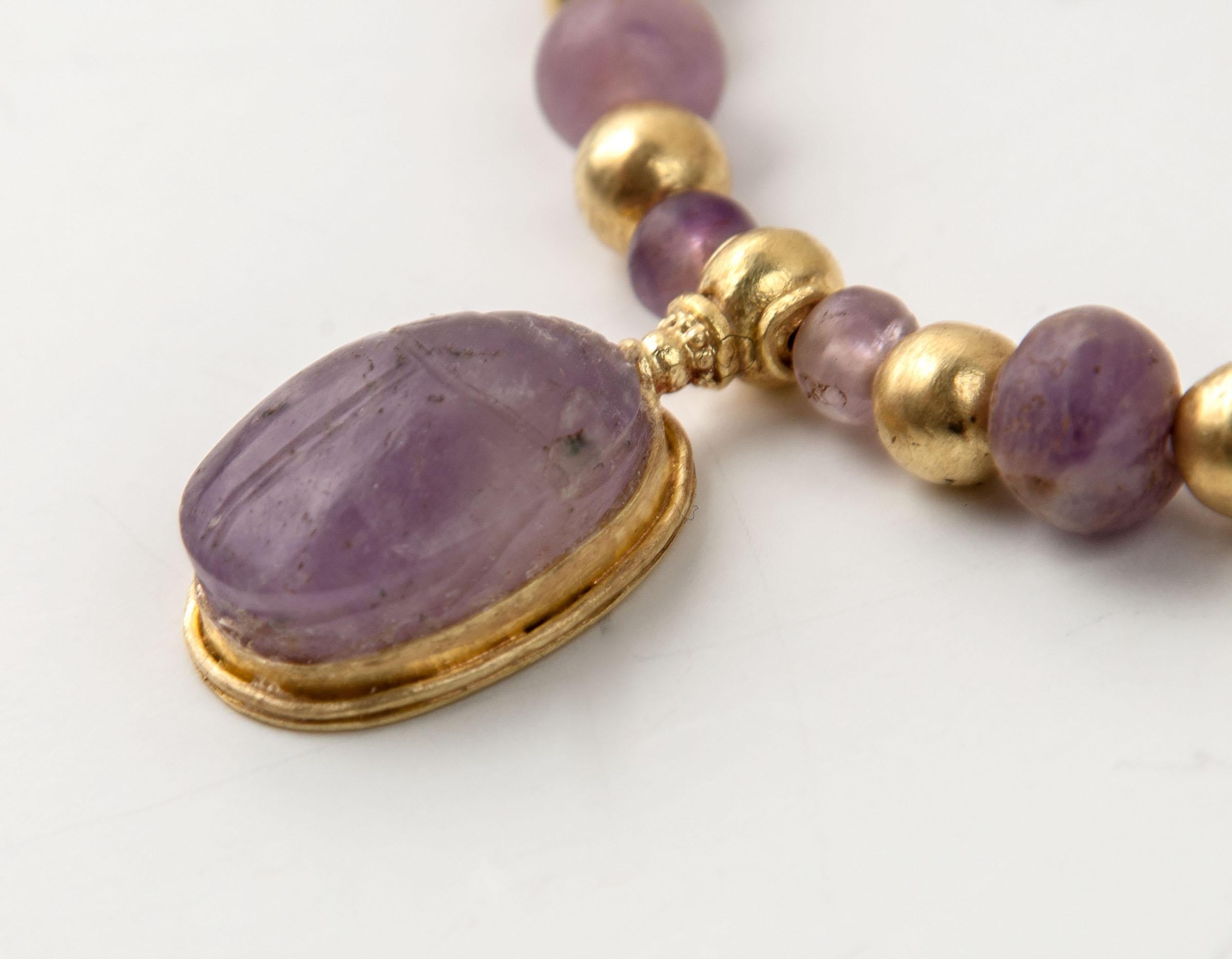 Collier de perles d'améthyste et de grenat de l'Égypte ancienne avec un pendentif scarabée en améthyste dans une monture en or. Il y a vingt-sept perles rondes d'améthyste et vingt-deux perles rondes de grenat dont la taille varie de l'avant à