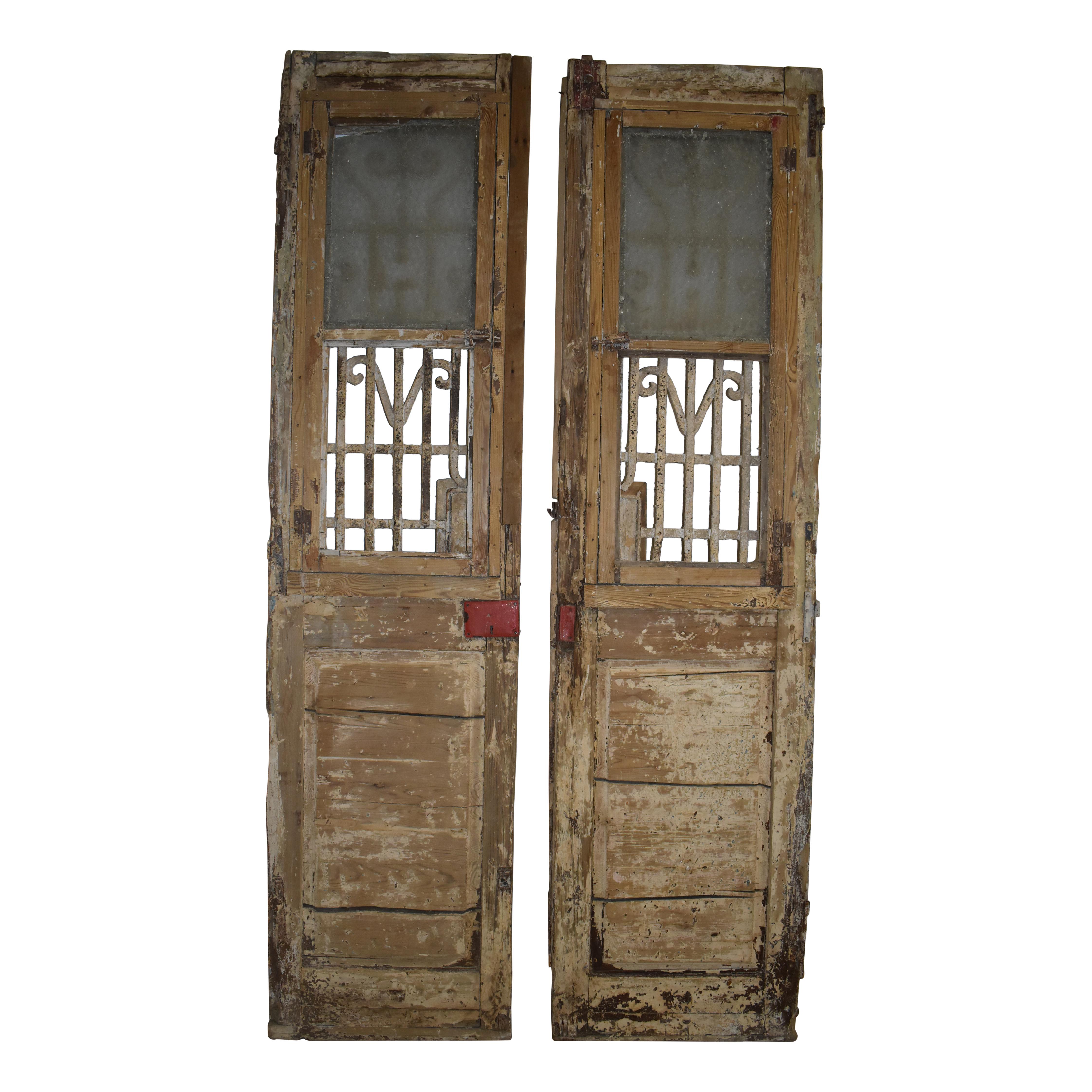 Made of Eastern European pine as is often the case in Egyptian doors, this beautiful set features raised panels on the lower half of each door with large window frames on the upper halves, enclosing decorative iron work. Most of the iron is riveted