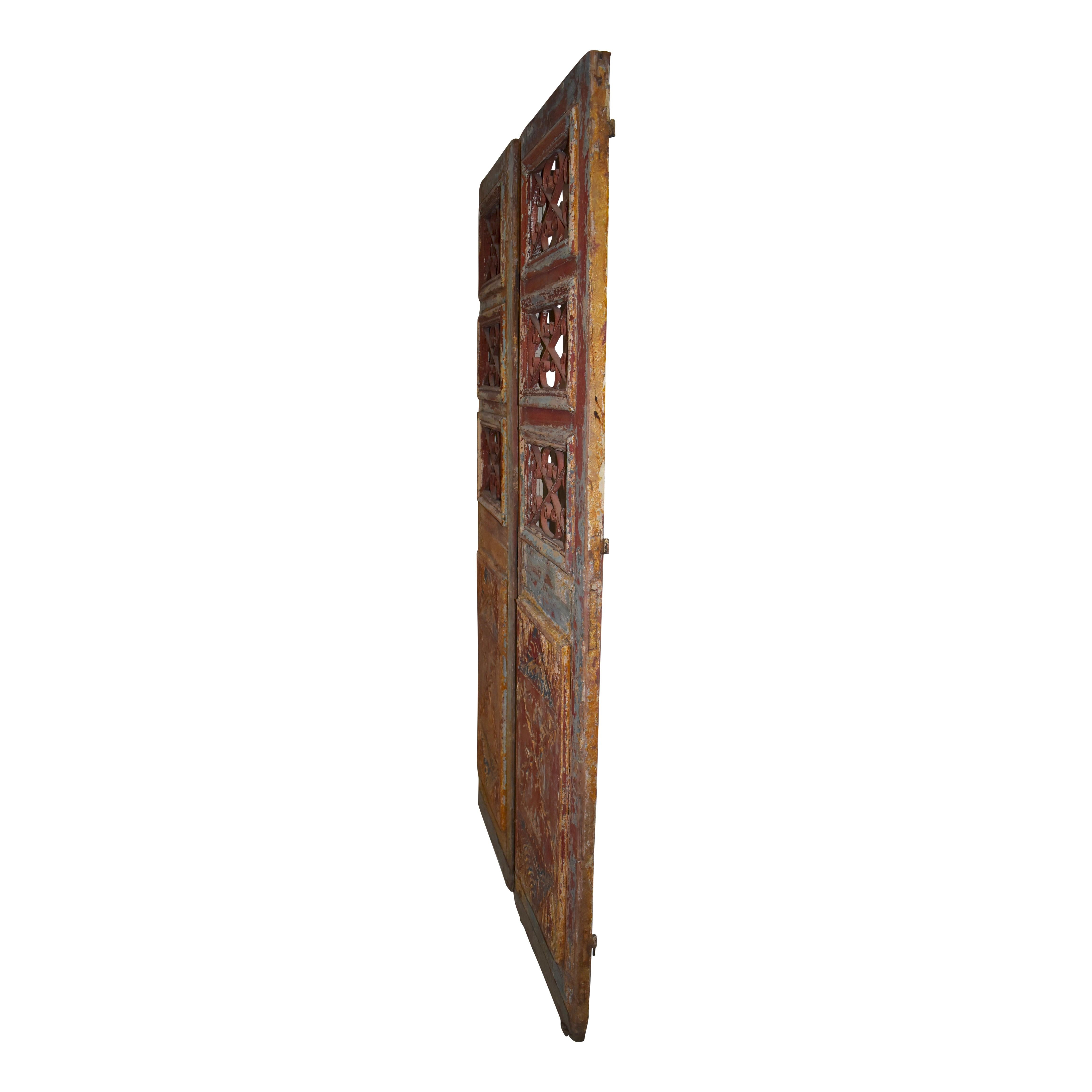 This set of Egyptian doors from the turn of the century is made of Eastern European pine. Each door has a carved panel on the lower half and three window frames inset with decorative metal on the upper half. One of doors has a portion of vintage