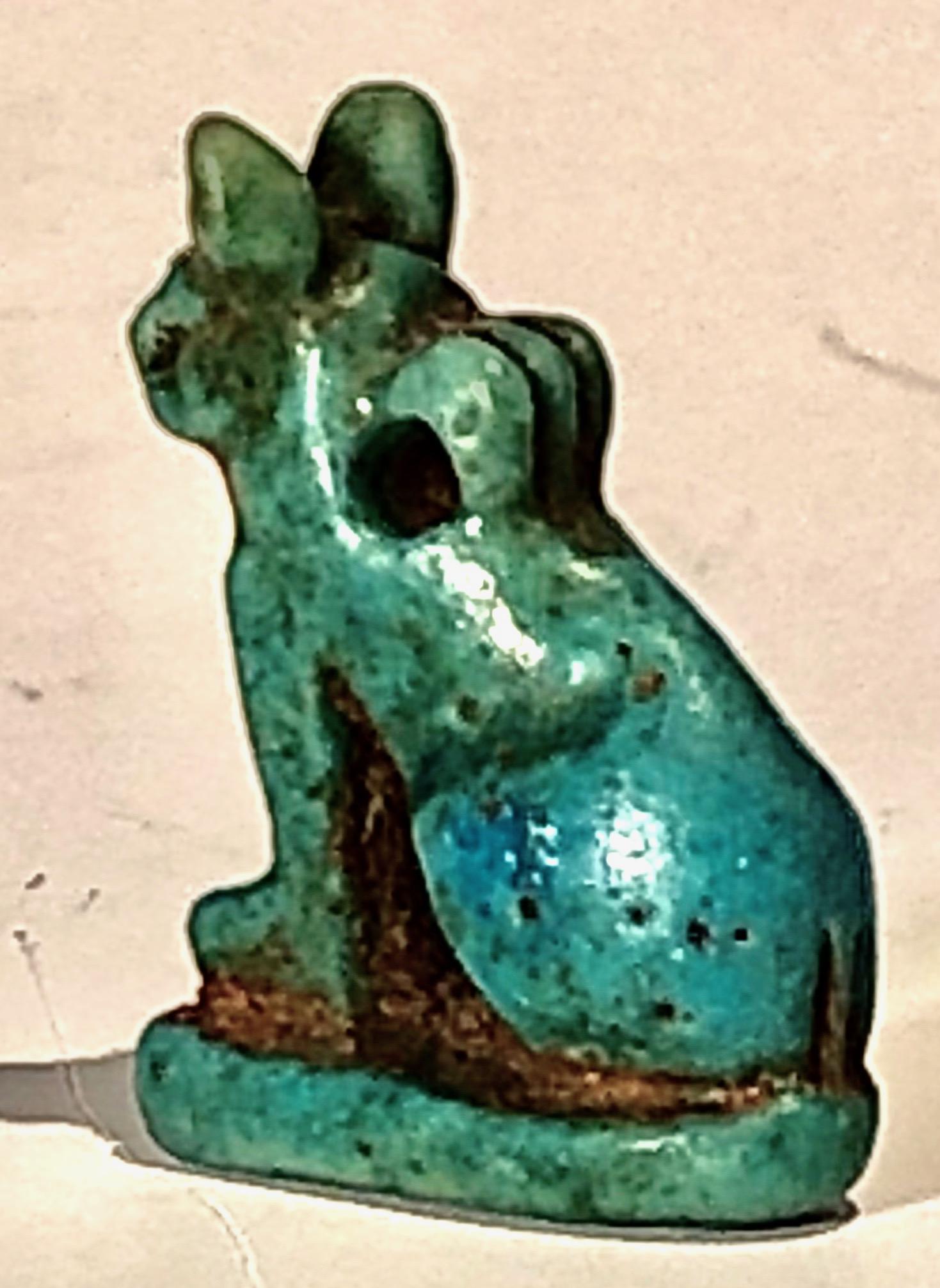 Egyptian blue glazed faience amulet of a cat. Third Intermediate Period, 1070-664 BC. Seated upon an integral plinth, the tail wrapped around its right side, a ridged suspension loop at the center of its back.
Amulets in the form of a cat represent