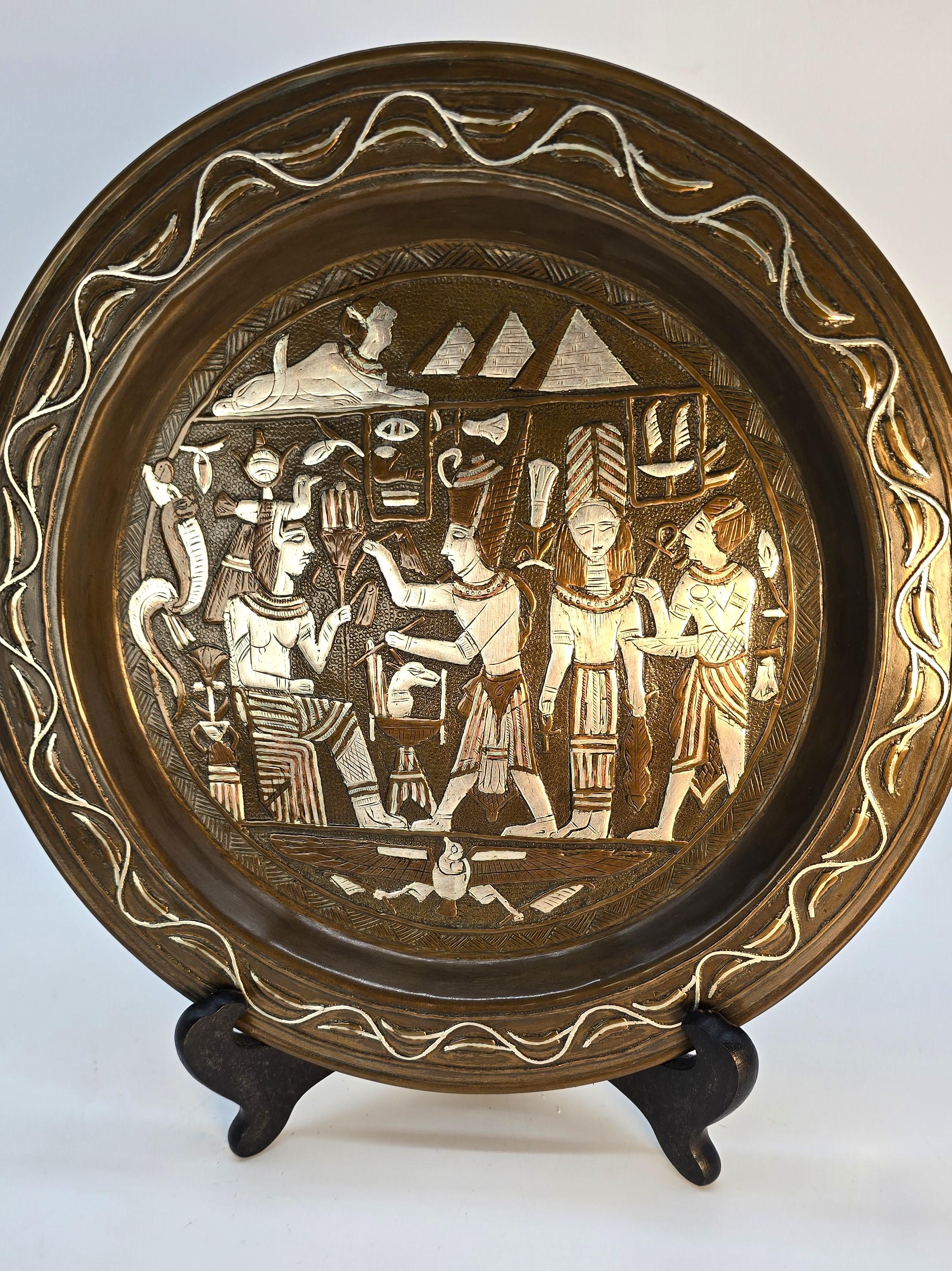 Questo superbo caricatore da parete Grand Tour egiziano è realizzato a mano in ottone o bronzo. Questo pezzo pregiato pesa più di mezzo chilo.

Il caricabatterie è molto decorativo. Al centro, presenta una complicata scena antica con figure