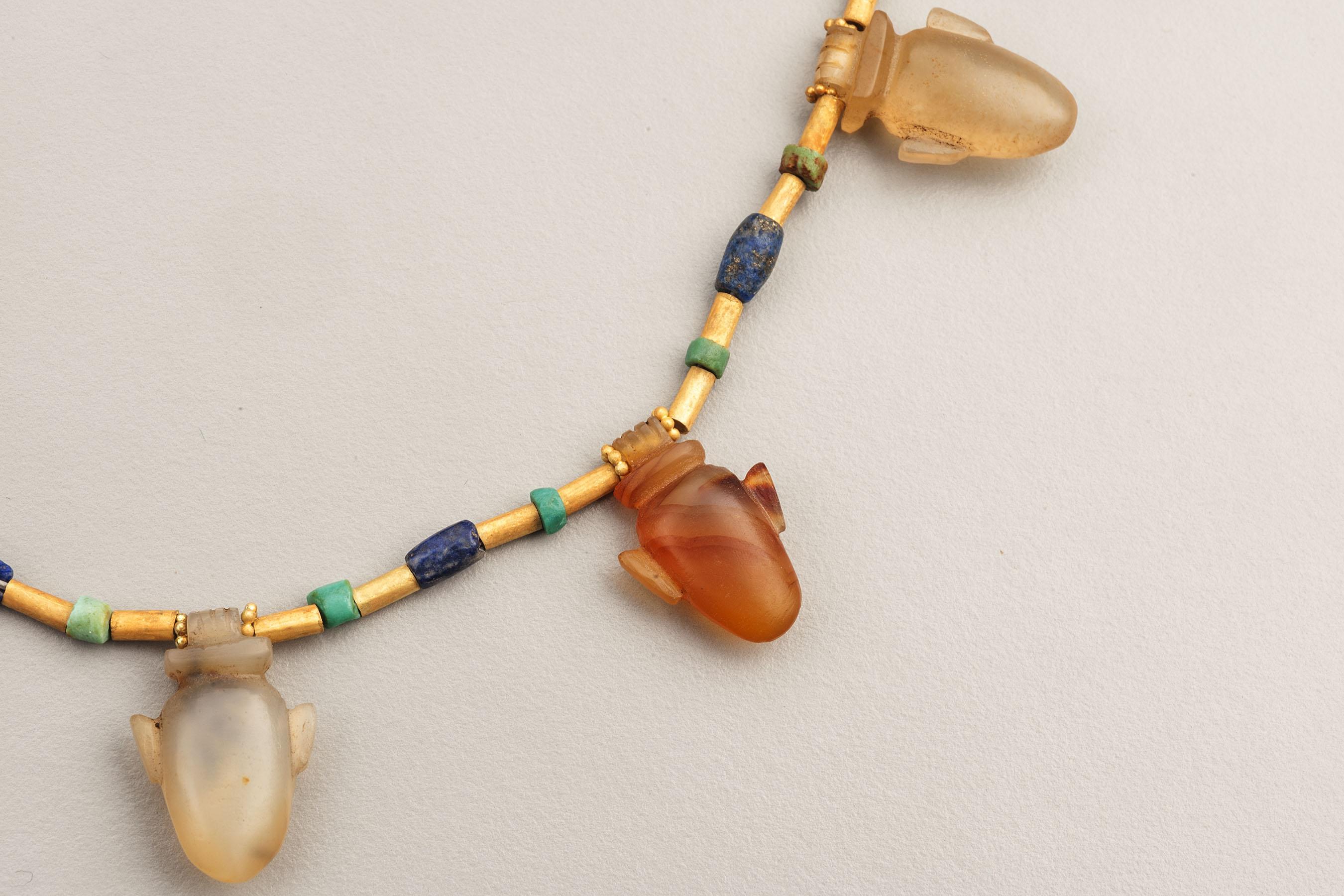 22k gold beads, turquoise and lapis lazuli beads with nine “heart” shaped amulets, most of which are grayish translucent quartz with varying amounts orange carnelian banding and three of which lack any orange color. The largest of these is 2 cm in