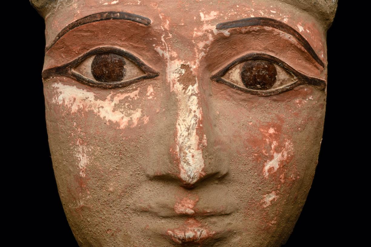 Carved hardwood mummy mask having a pink-brown painted ground, painted black eyes and brows. Wearing a black headband. Eyes and brows are restored. Scattered highpoint paint wear, otherwise intact.

Provenance: Sold to Ezeldeen Taha Eldarir from