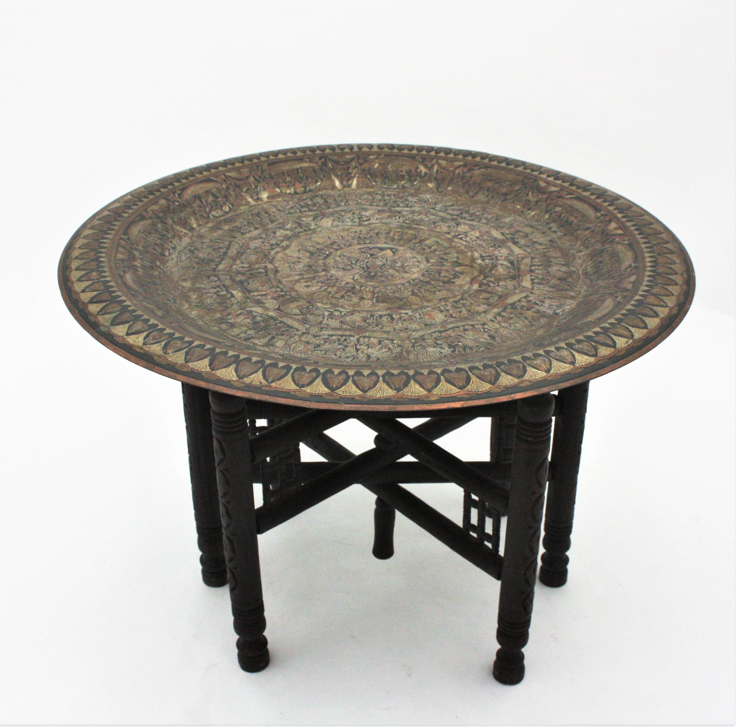 Large egyptian brass tray table with wood folding base, 1950s
The removable round bras top has a very detailed hand engraved decoration with polychrome egyptian designs. It stands up on a wooden carved folding base with 6 turned legs.
Very fine and