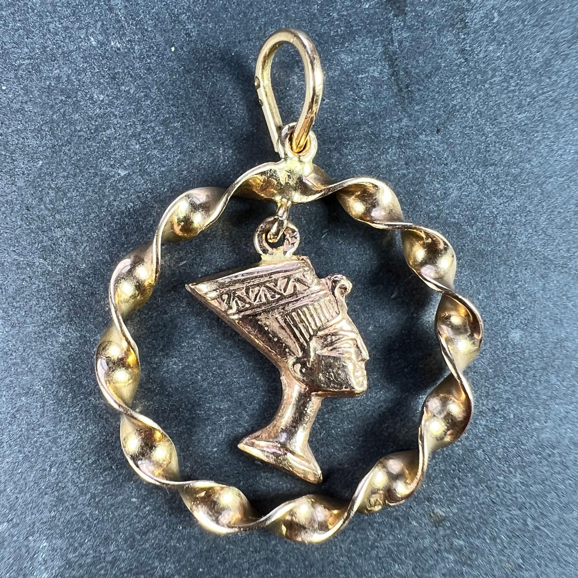 An Egyptian 18 karat (18K) yellow gold charm pendant designed as a bust of the head of Queen Nefertiti within a twisted gold circle. Stamped with the Egyptian mark for 18 karat gold.

Dimensions: 2.7 x 2.4 x 0.3 cm (not including jump ring)
Weight: