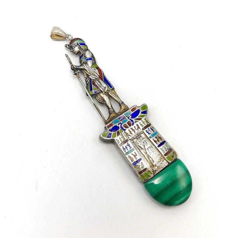 This is an interesting Egyptian Revival Figurative Pendant. Standing atop a building covered with hieroglyphs, an Egyptian male stands erect holding a staff in one hand and an Ankh in the other.  There is a doorway or passage with a palm tree