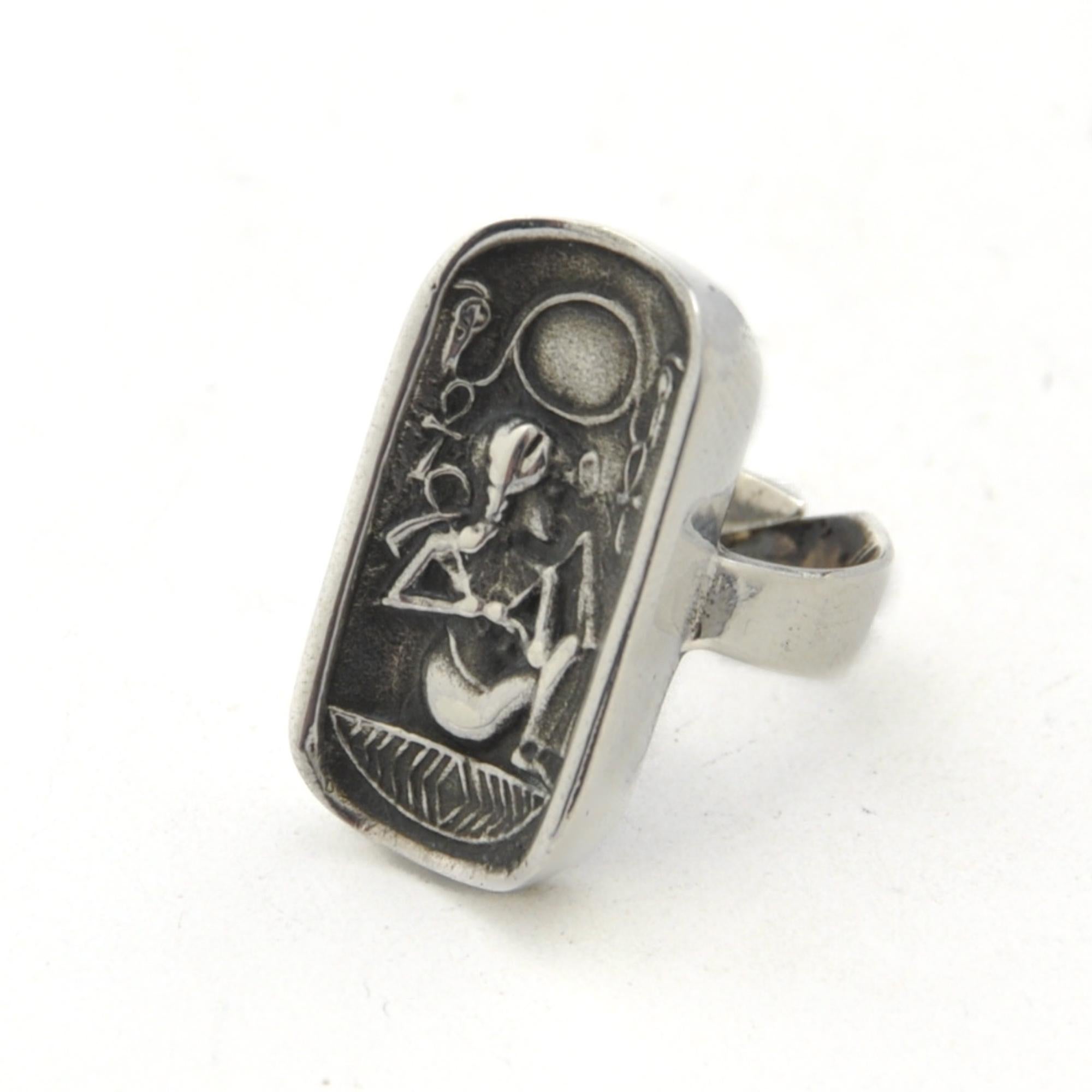 A beautiful Egyptian Revival cartouche ring depicting a sitting pharaoh with Egyptian symbols. The pharaoh is holding a crook and flail in his hands, these were symbols of the pharaoh, the ruling monarch in Ancient Egypt. The crook and flail