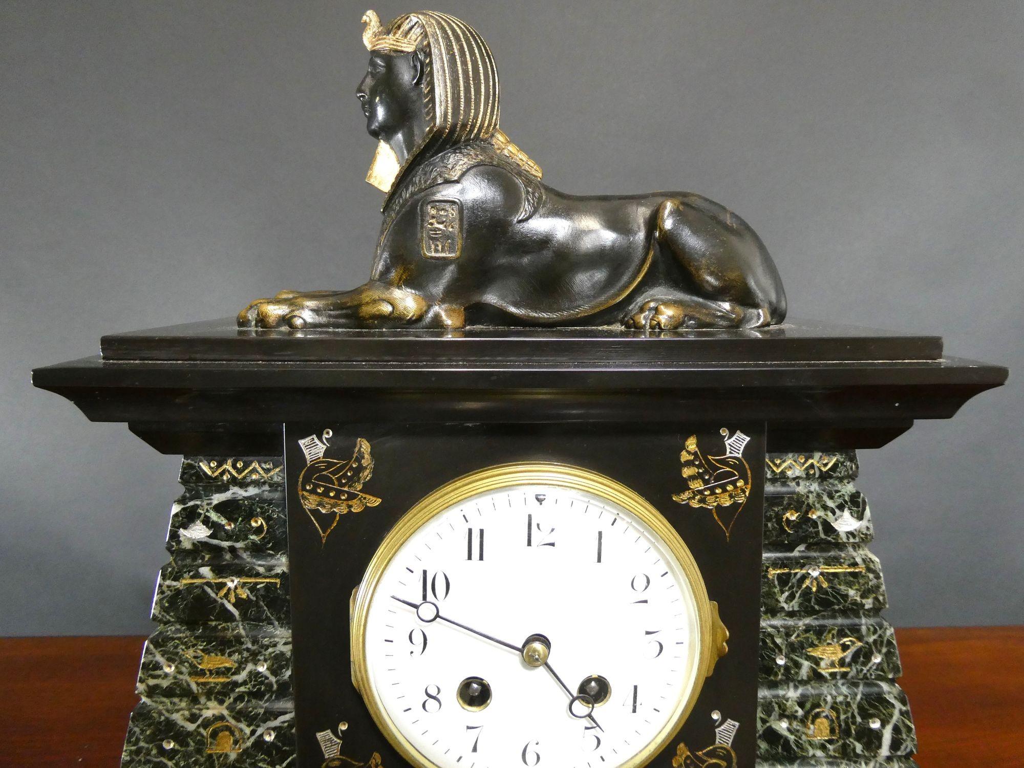 Egyptian Revival Bronze and Marble Mantel Clock

Egyptian revival mantel clock housed in a polishes black slate and marble stepped case, decorated with winged uraeus and hieroglyphs, surmounted by a patinated bronze sphinx wearing nemes and resting