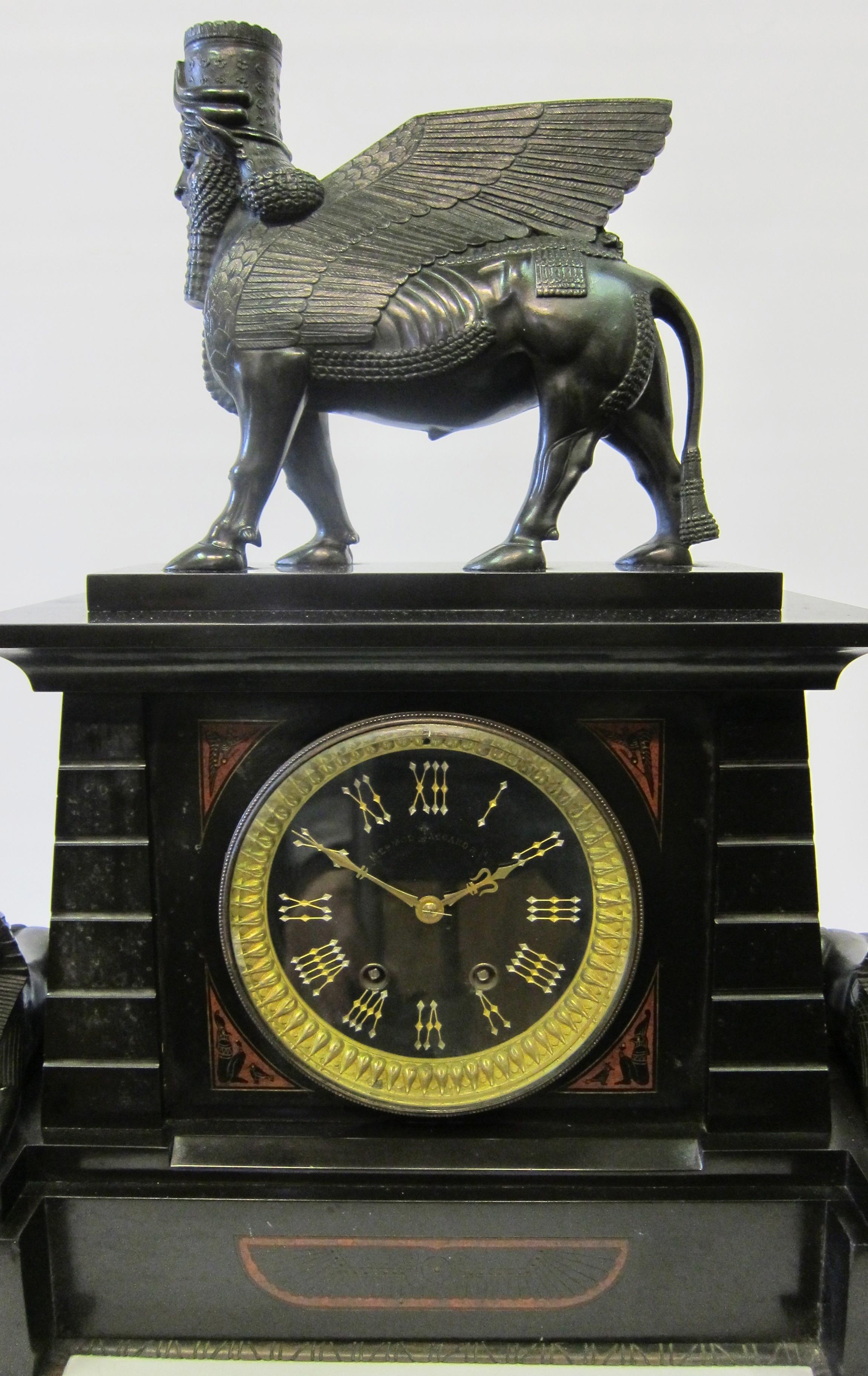 This wonderful 1920s Egyptian Revival clock is surmounted with an Assyrian style lamassau (human headed winged lion) and flanked by a pair of reclining sphinx. The clock case etc. is made of black marble and decorated with faux hieroglyphics and