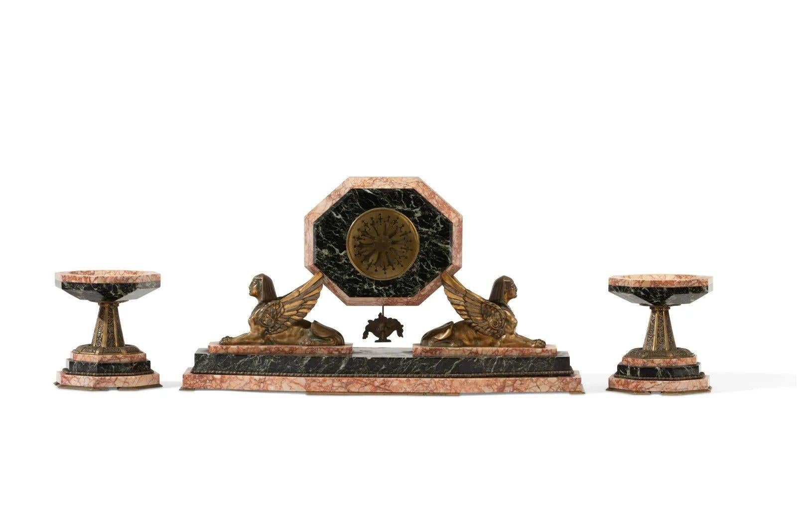 An Art Deco Egyptian Revival clock set
Early 20th century; France
Metal dial with black Arabic numerals set in a two-tone marble case flanked by bronze sphinxes, with matching compotes
3 pieces
Clock: 13