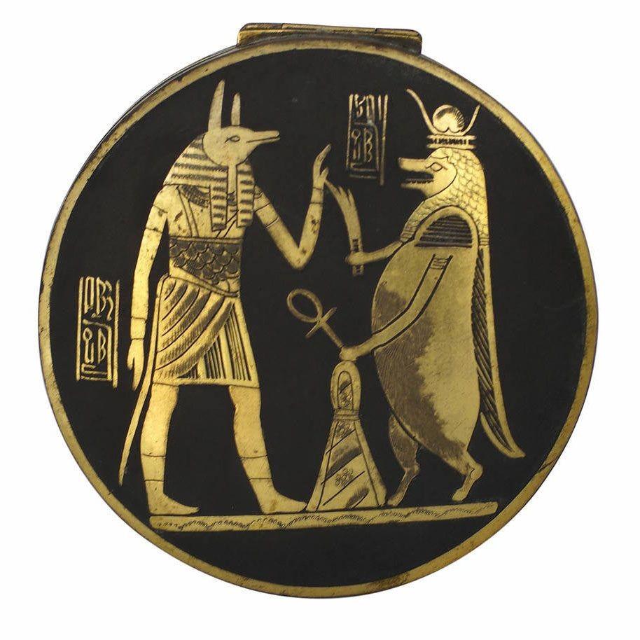 Cette pièce est un coffret décoratif en damasquinerie de style néo-égyptien, avec une finition en plaques d'or et des hiéroglyphes égyptiens le long du couvercle et des côtés, avec des détails gravés à la main, fabriqué vers 1920. Le couvercle est