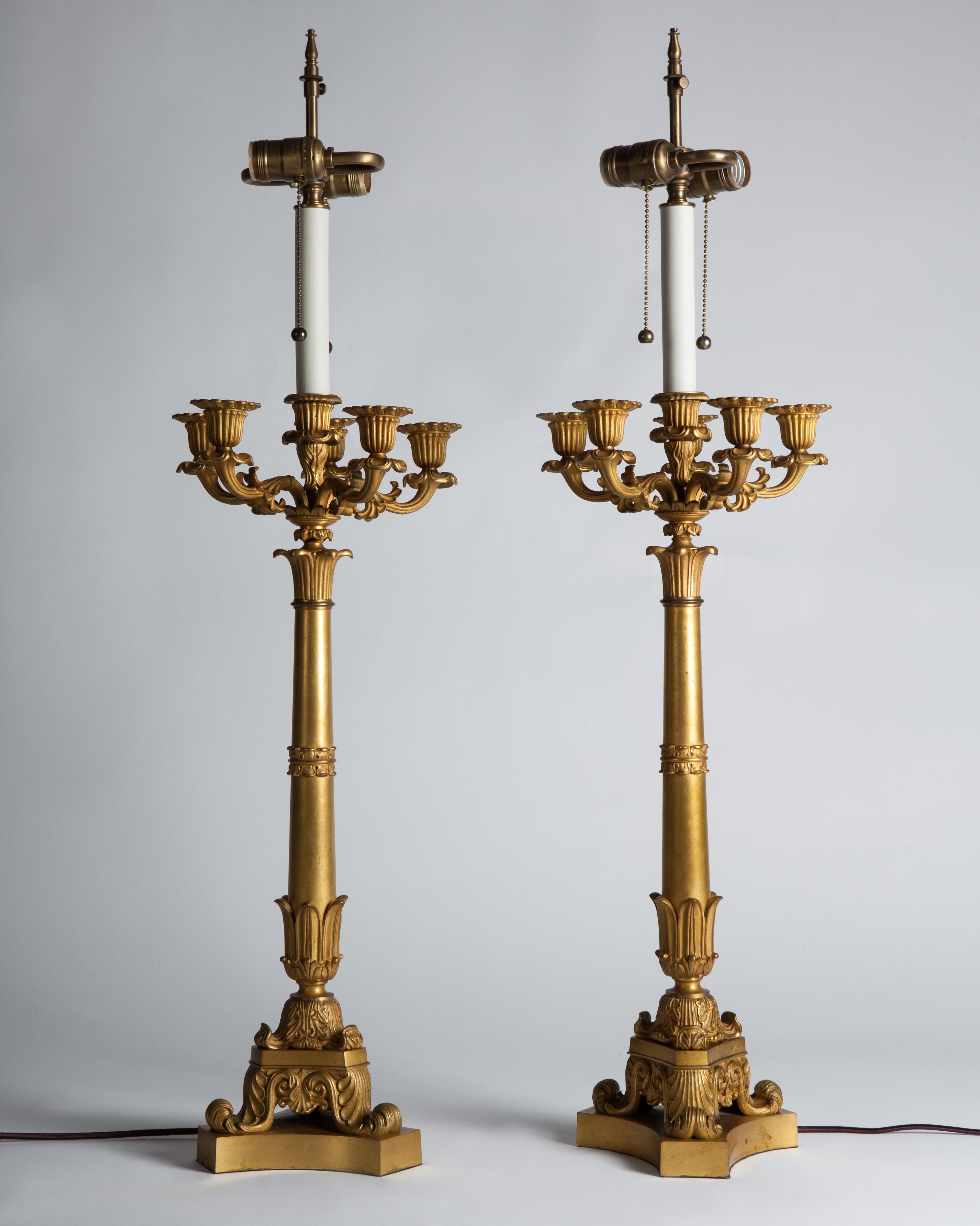 A pair of Egyptian Revival vintage bronze table lamps in their original very Fine gilded finish consisting of a tripod base holding a column crowned with six foliate arms, circa 1840. Converted to electricity in the 20th