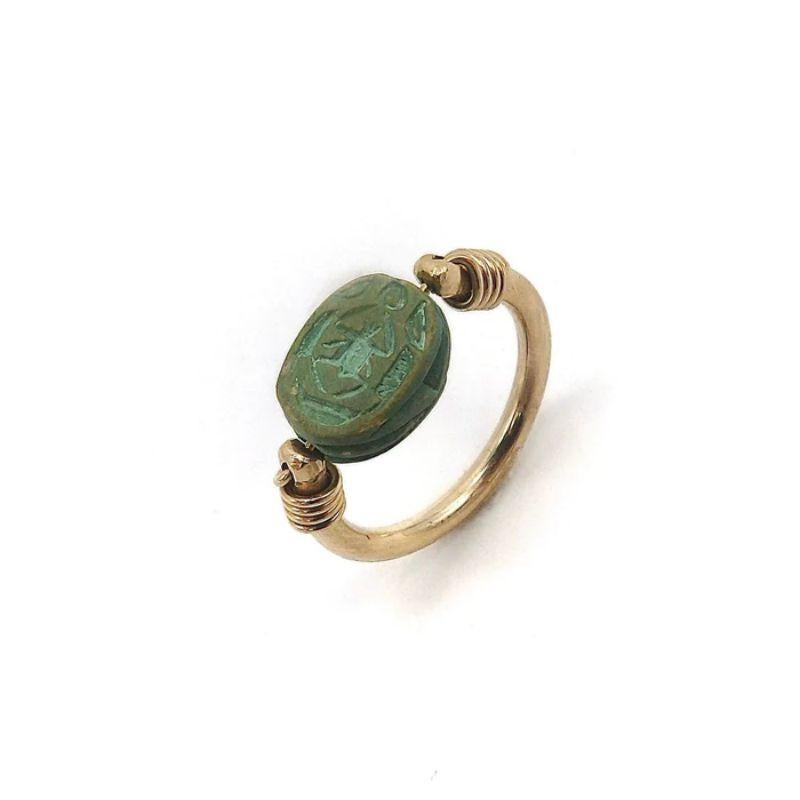 Egyptian Revival gold ring featuring a green Egyptian paste scarab. Egyptian paste was a self glazing clay used to make such scarabs and other artifacts. The gold spiral wire on the band is wound around the shoulders and through the convex terminals