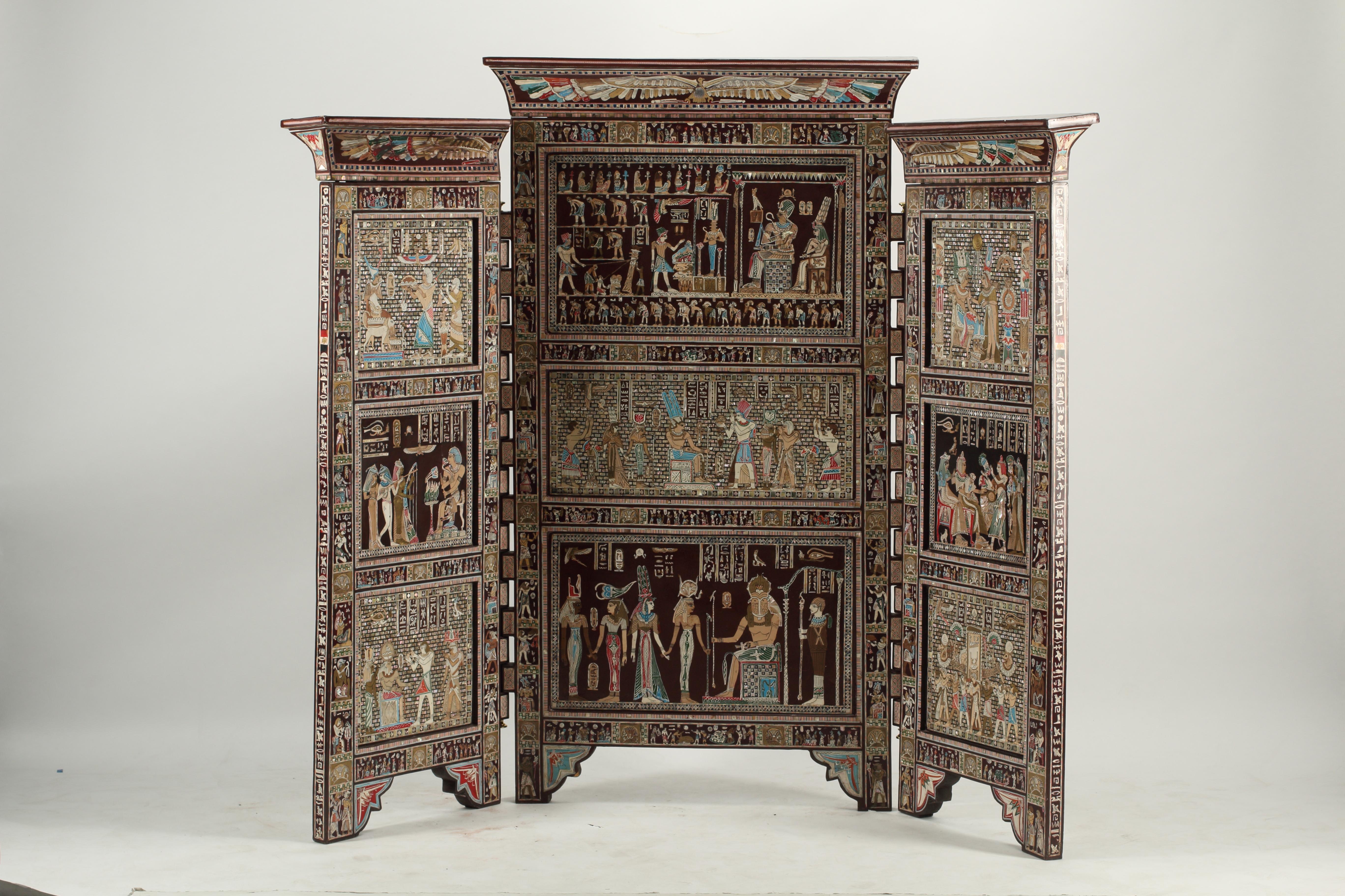 A remarkable three-panel, double faced Egyptian Revival screen that displays the iconic motifs of ancient Egypt with masterfully inlaid and hand-painted scenes. Each panel is adorned with depictions of pharaohs, hieroglyphics, deities, and