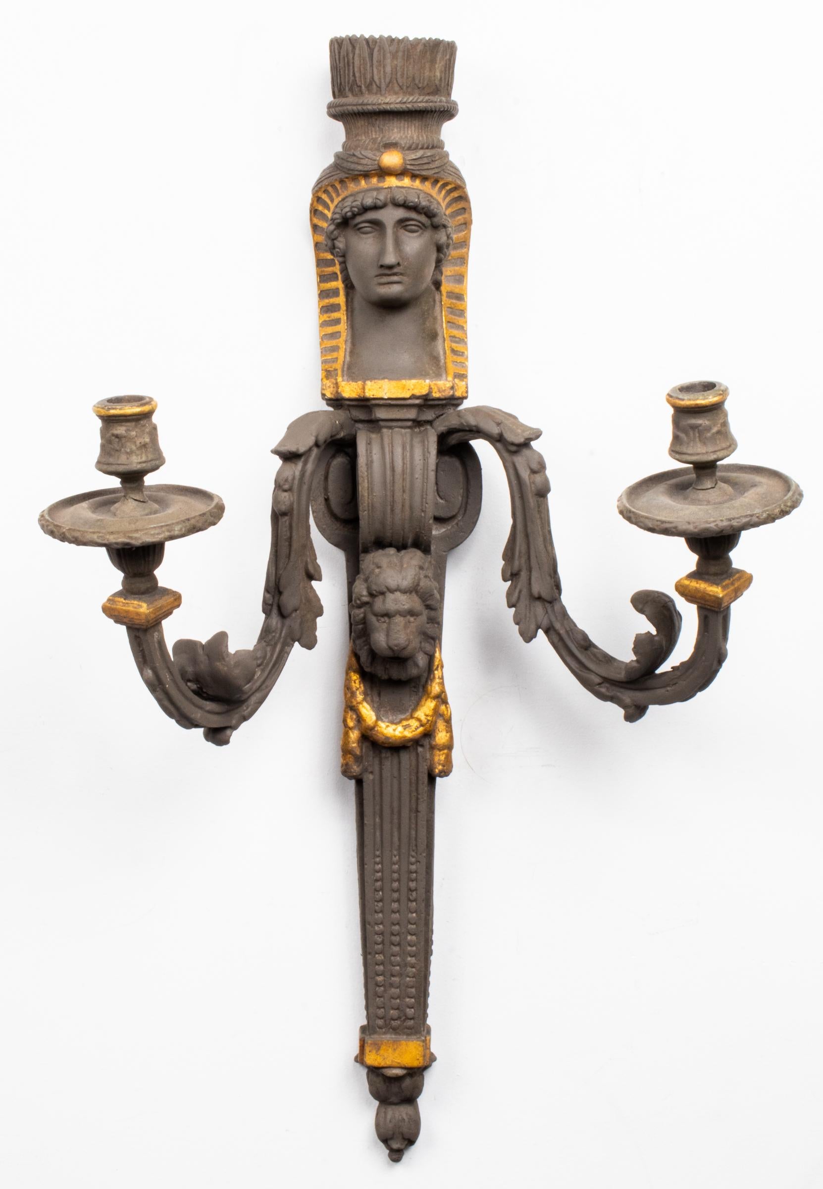 Large pair of Egyptian Revival manner two-light sconces, 20th century, overall paint and gilt decorated, the figures with elaborate headdresses above two scrolling arms flanking a lion mask on the tapered columns. Measures: 30.5” H x 18” W x 10” D.