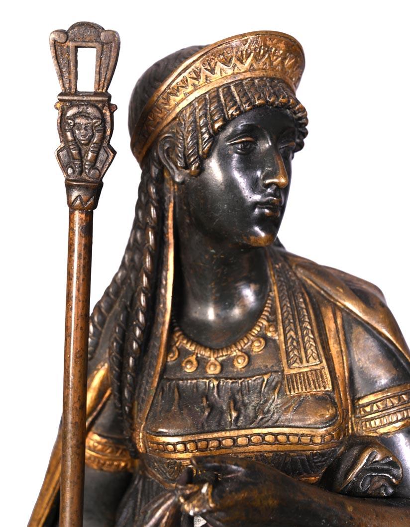 Mantel clock in patinated and gilt bronze, with red and black marble, in the Egyptian Revival style of the 19th century. 
The composition features a standing female Egyptian figure holding a staff, positioned atop a flared pyramidal base. The
